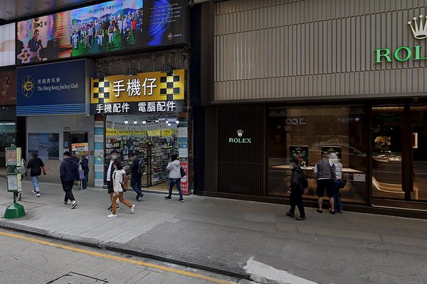 Pedestrians walk past stores on Nathan Road in Mong Kok, including a Rolex store and one with noticeable yellow signage.