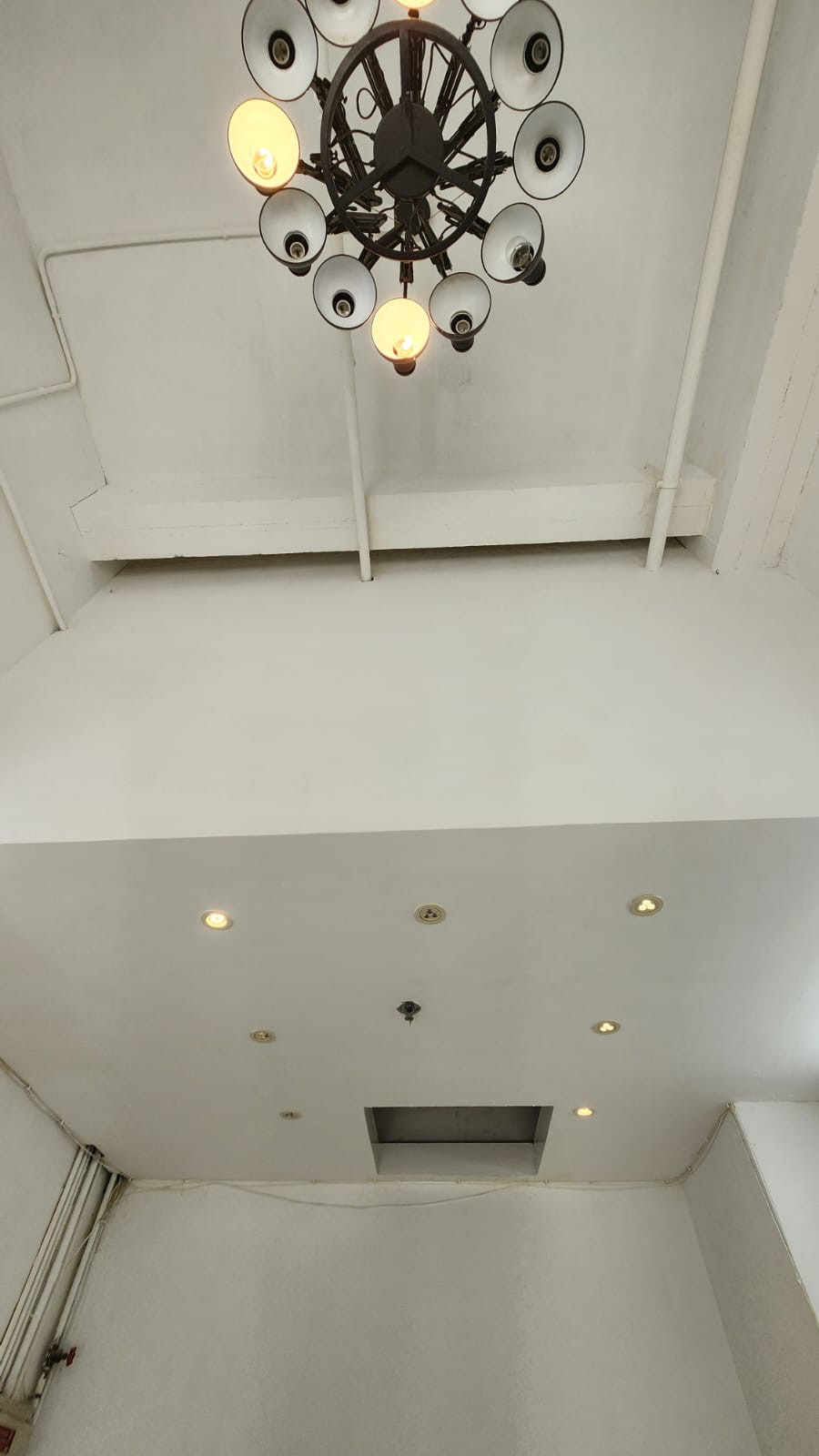Black chandelier with round lights hangs from a white ceiling with exposed pipes in a Sai Ying Pun Third Street flat.