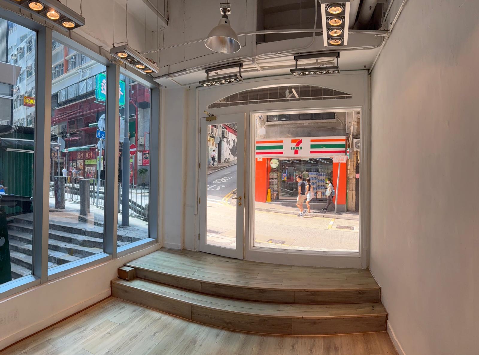 Empty room with wooden floor, steps, and large windows on Queen’s Road Central, facing a 7-Eleven store.