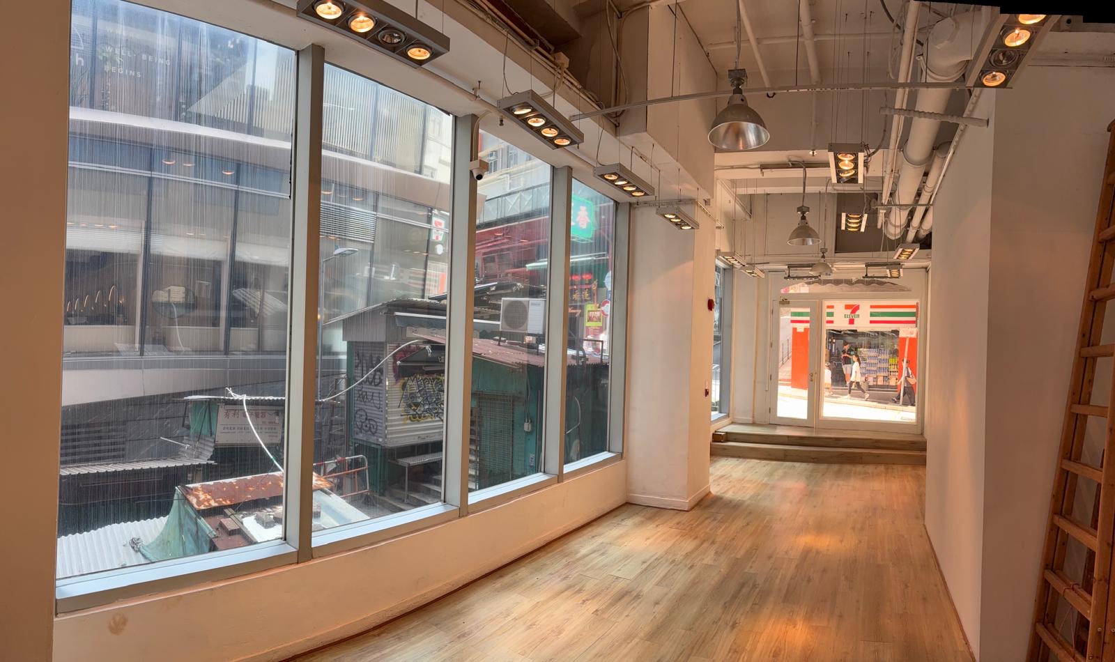 Empty hallway with wood floors and large windows overlooking Queen’s Road Central and the city street outside.