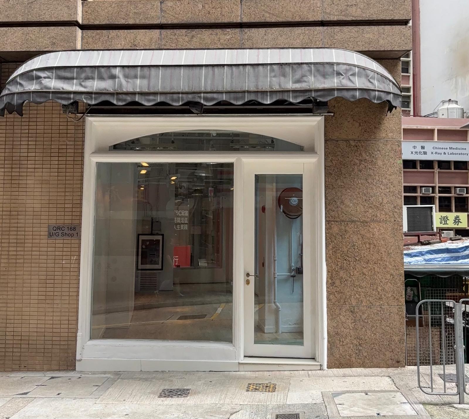 Closed shop on Queen’s Road Central with a glass door, white frame, gray striped awning, and tiled wall.
