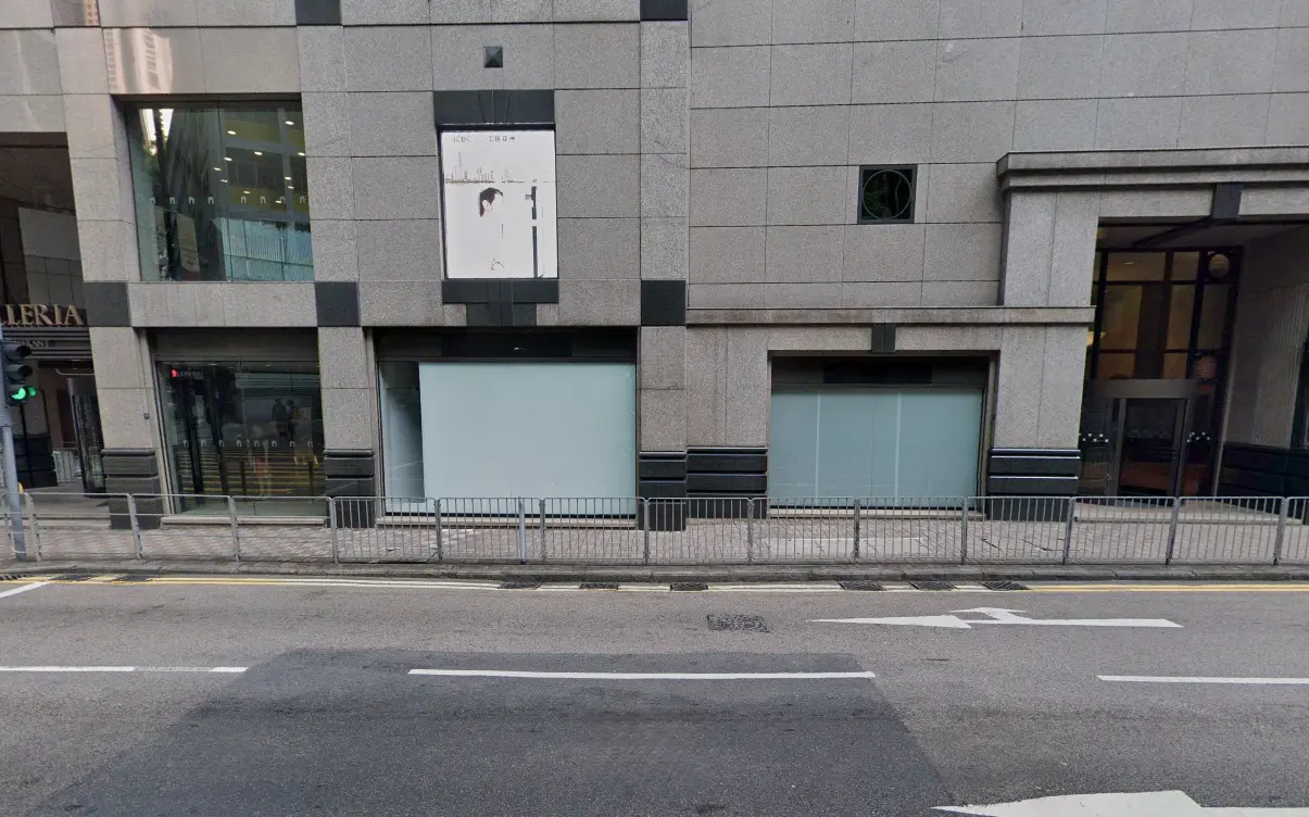 Shop on Queen's Road Central, Central. Gray building with large windows on Queen’s Road Central, metal railings in front, and lane markings on the road.