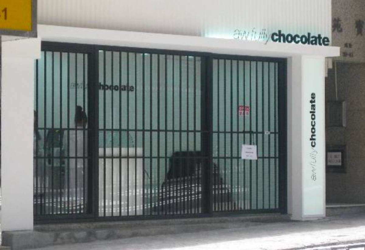 Storefront on Caine Road with large barred gates, glass doors, and Awfully Chocolate signage; closed sign on the gate.