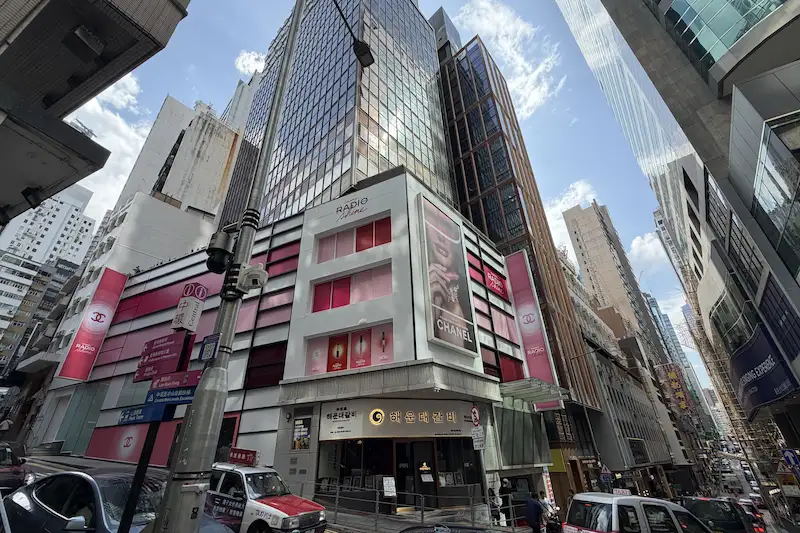 Tall glass buildings in Hong Kong with colorful shop signs and cars on the street.