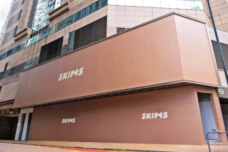 A beige SKIMS building with white letters is on a city street near Times Square in Hong Kong.