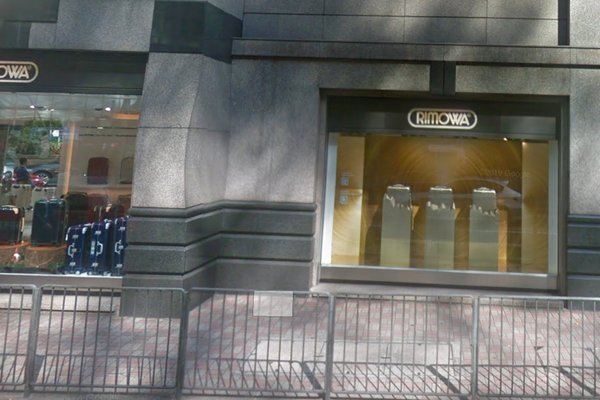 中環皇后大道中舖位。一間RIMOWA舖面,櫥窗展示行李箱,人行道外設有金屬圍欄。