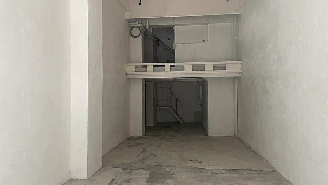 狹窄空置房間鋪設混凝土地面，牆身雪白，後方設有閣樓及樓梯。