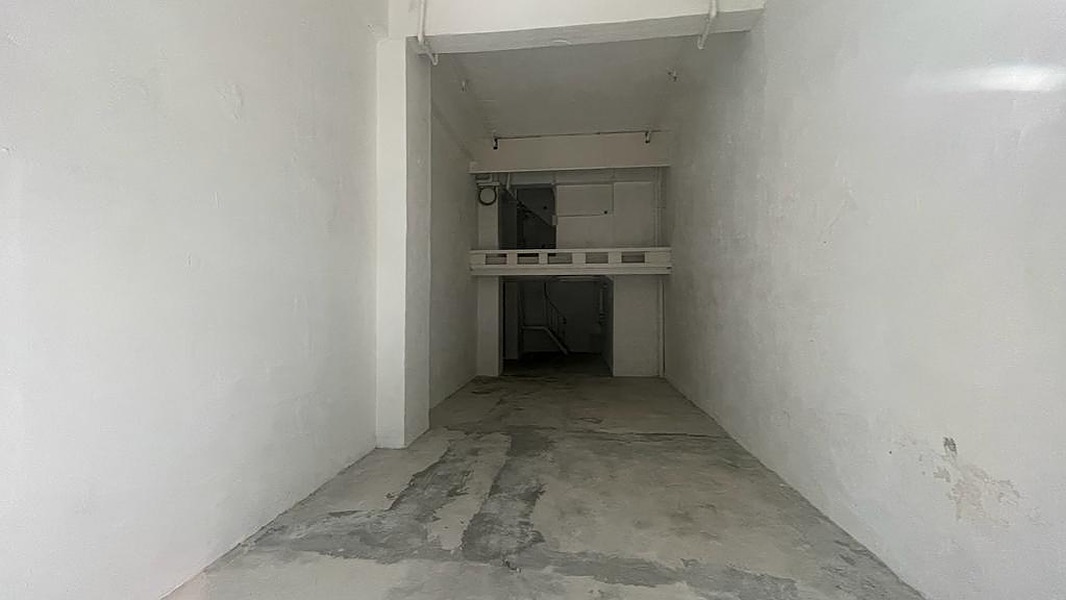 狹窄空置房間牆身雪白，鋪設混凝土地面，後方低層空間上方設有小型閣樓。