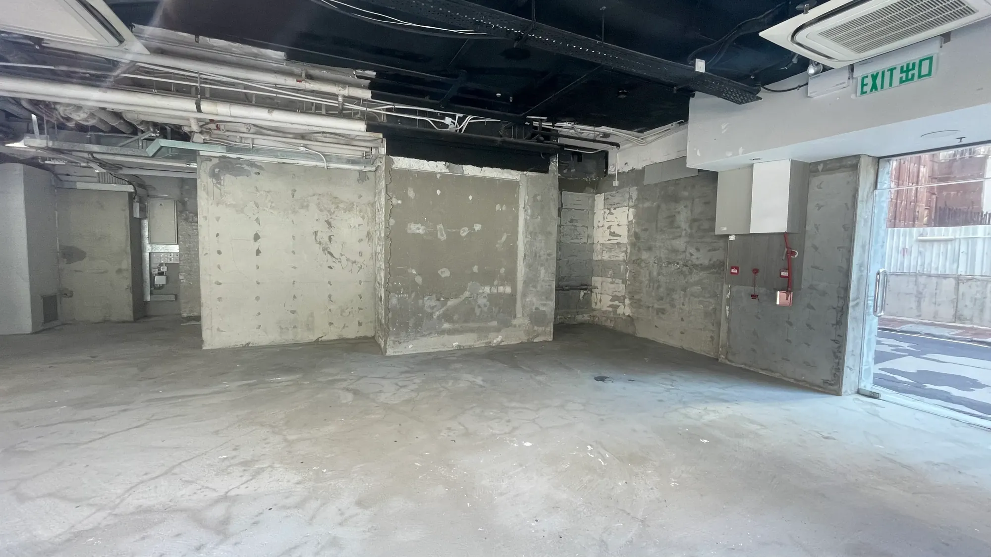 堅拿道東一個空置工業單位牆身混凝土，喉管外露，設火警鐘及玻璃門上方EXIT標示。