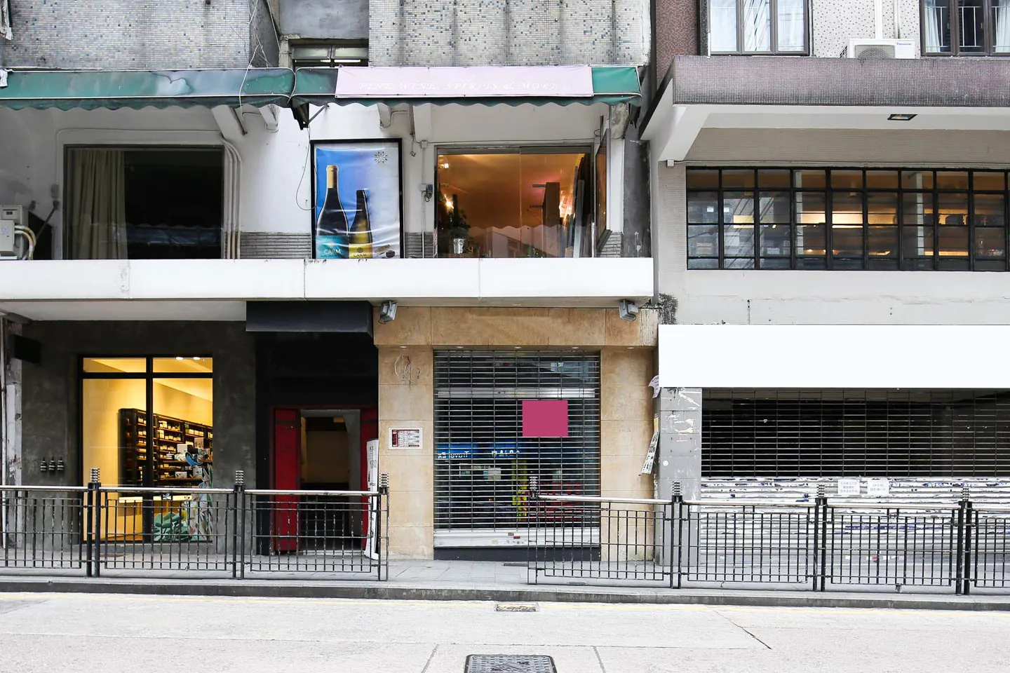 Three closed storefronts with metal shutters on Hollywood Road in Central, buildings visible behind them.