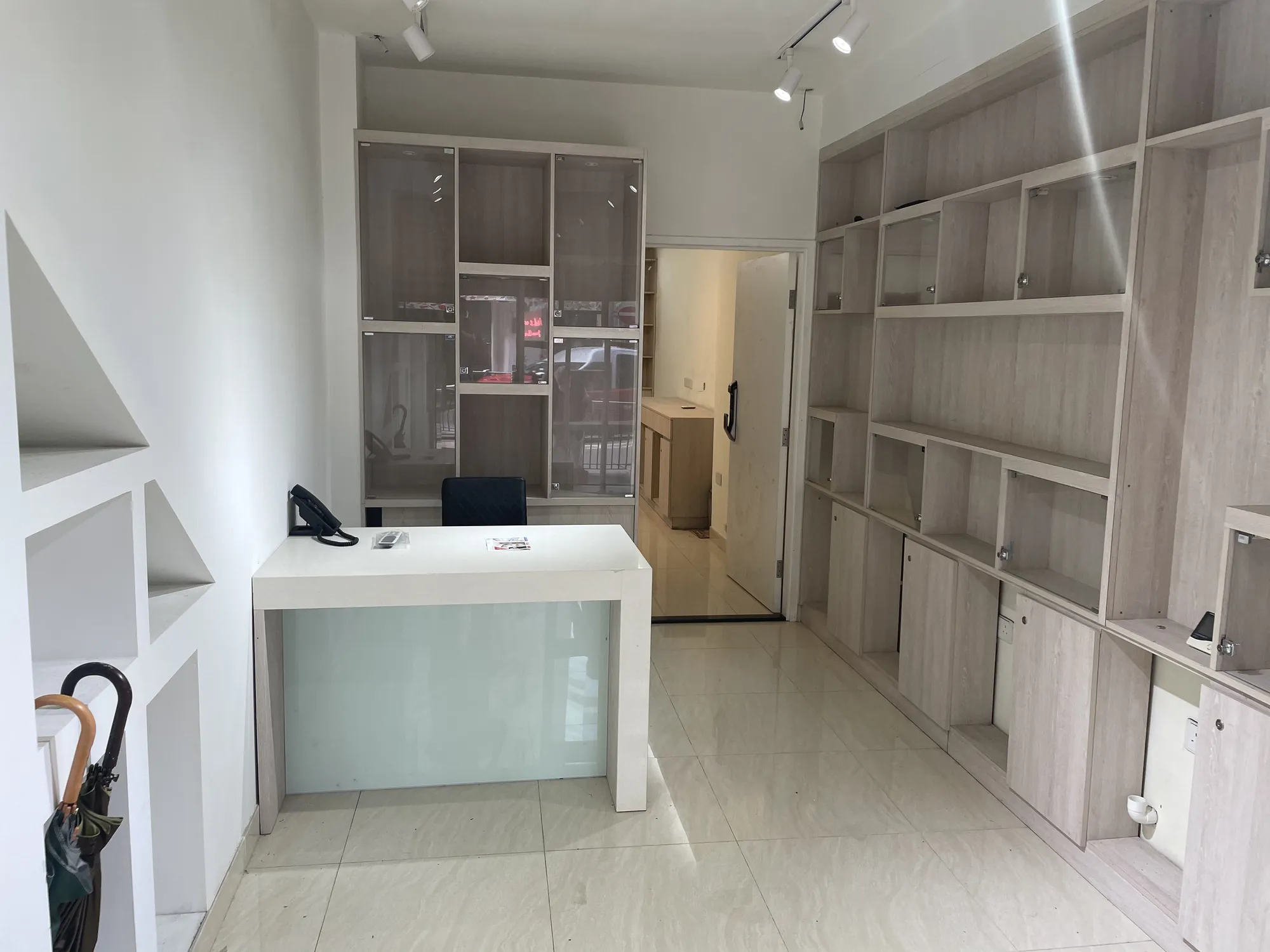 Minimalist office on Hollywood Road Central with a white desk chair open shelves and an umbrella in the corner.