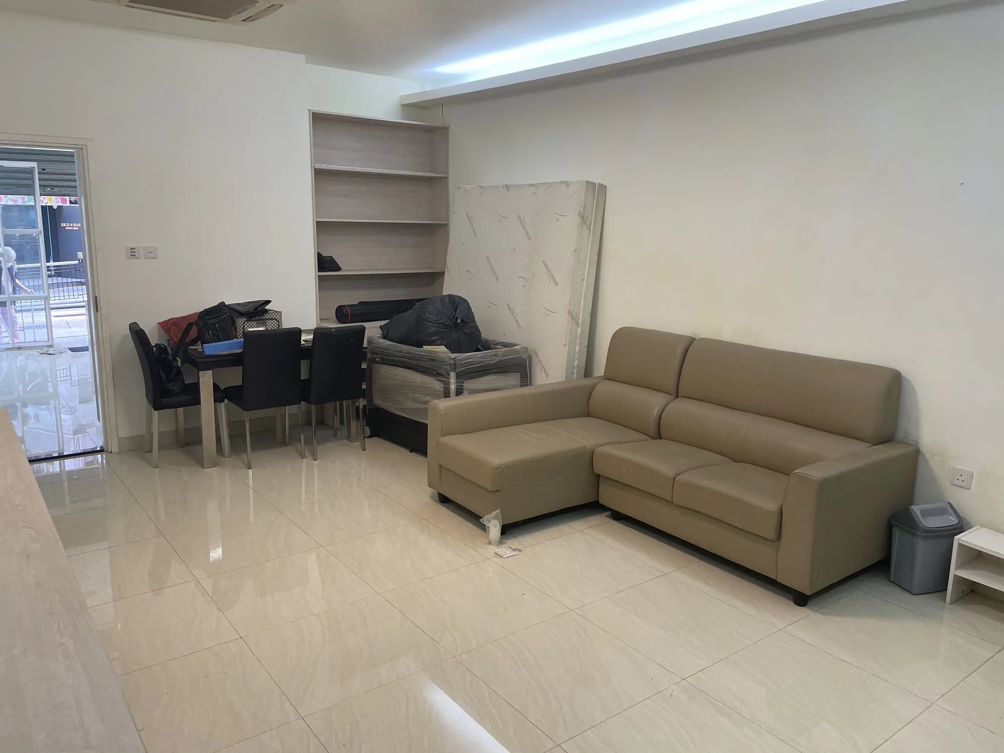 A beige sofa, dining set, and mattress in a tiled Central living room on Hollywood Road with clutter and an empty shelf.
