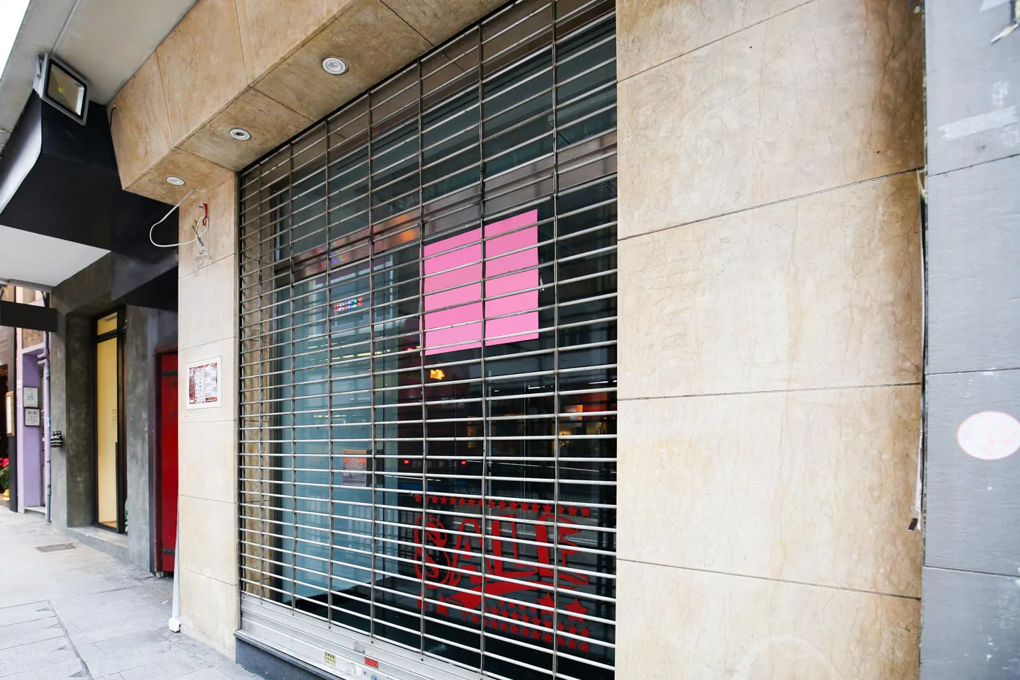 A closed storefront with a metal security gate and a pink sign on the window along Hollywood Road, Central.