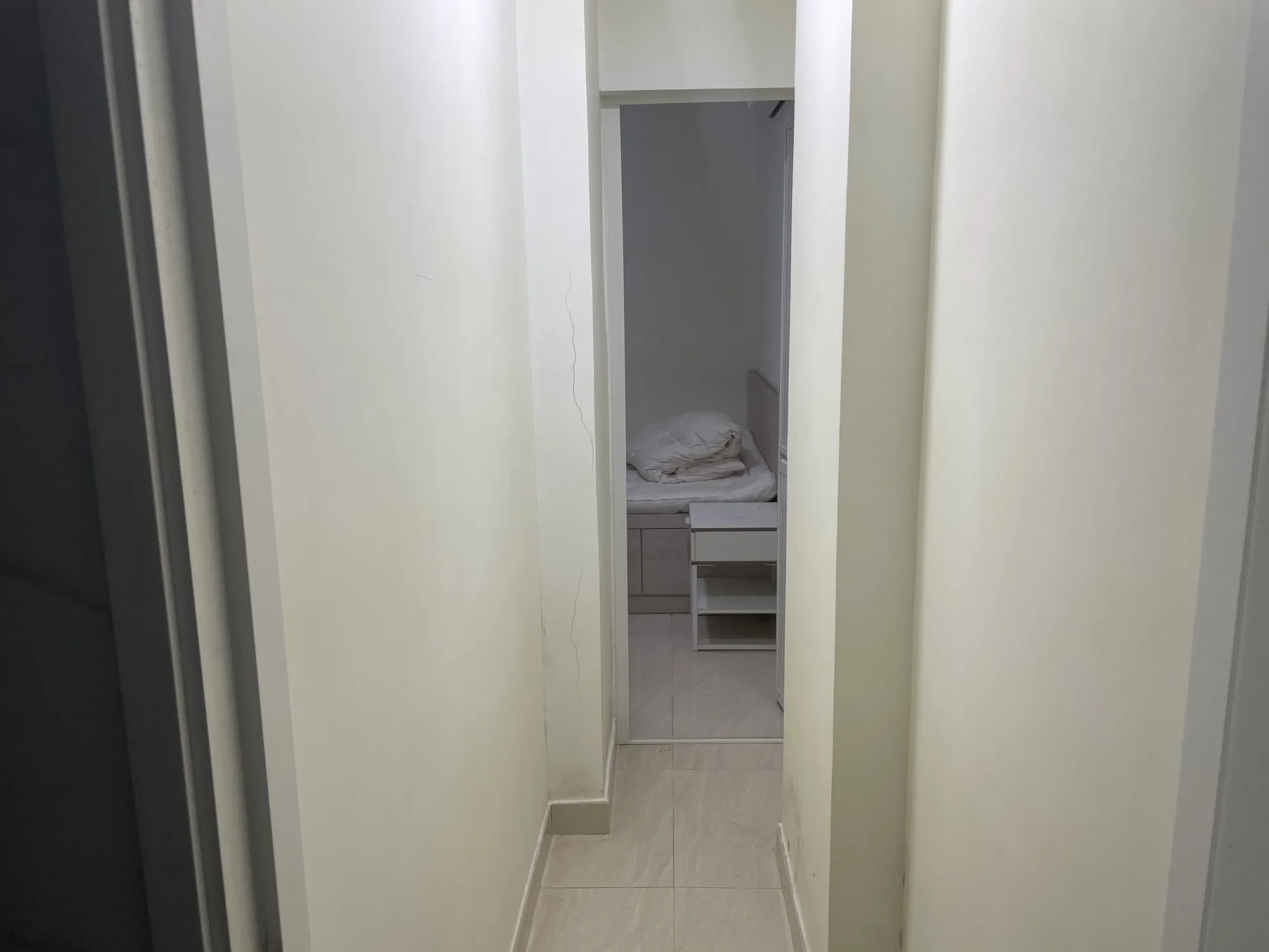 Narrow hallway with light walls on Hollywood Road Central leads to a small bedroom furnished with a bed and nightstand.