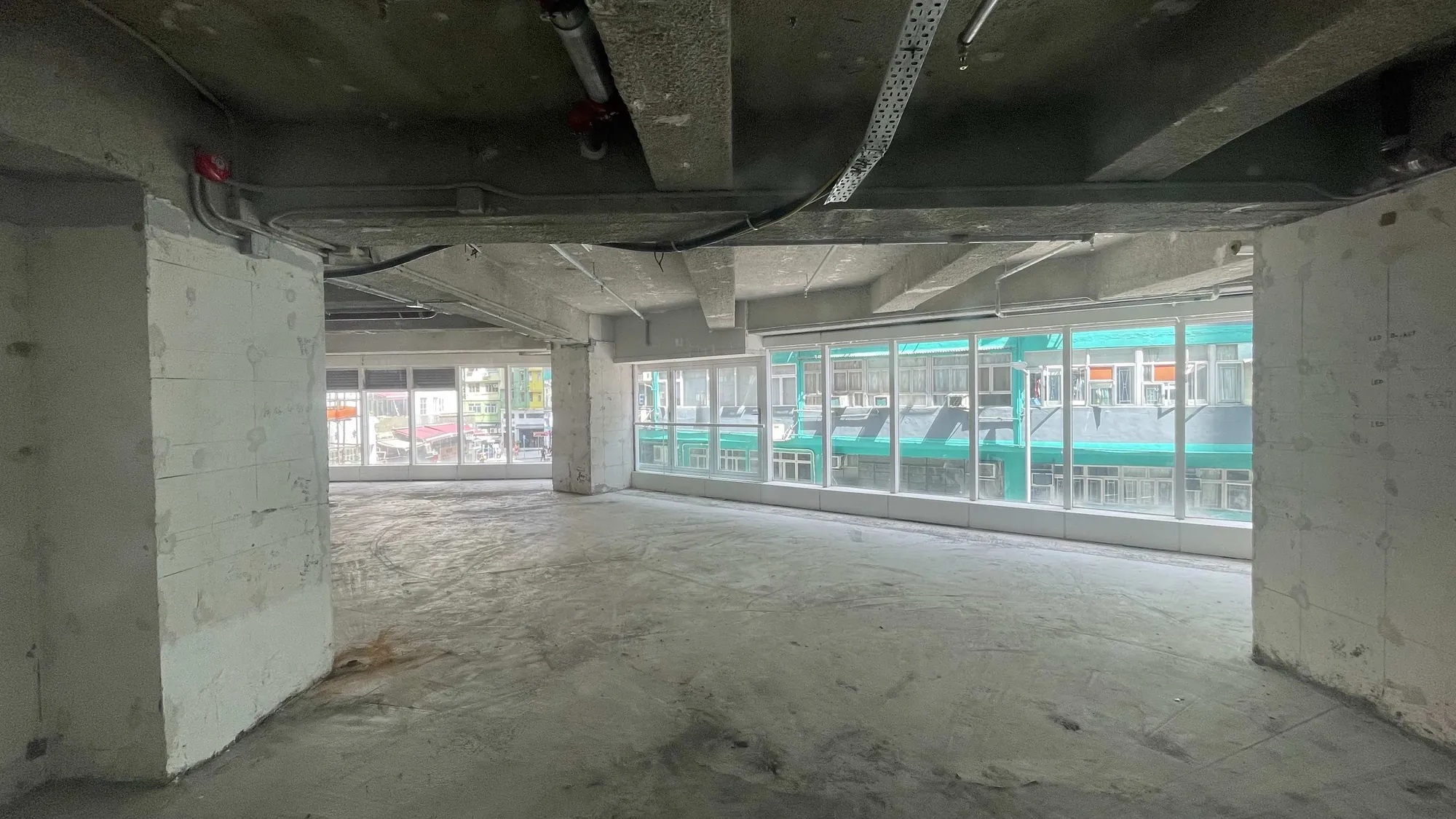 Ref#2990: Spacious, unfinished room with concrete floors, exposed ceilings, and large windows perfect to rent as an office or shop. Enjoy city street views and green awnings visible through the windows.