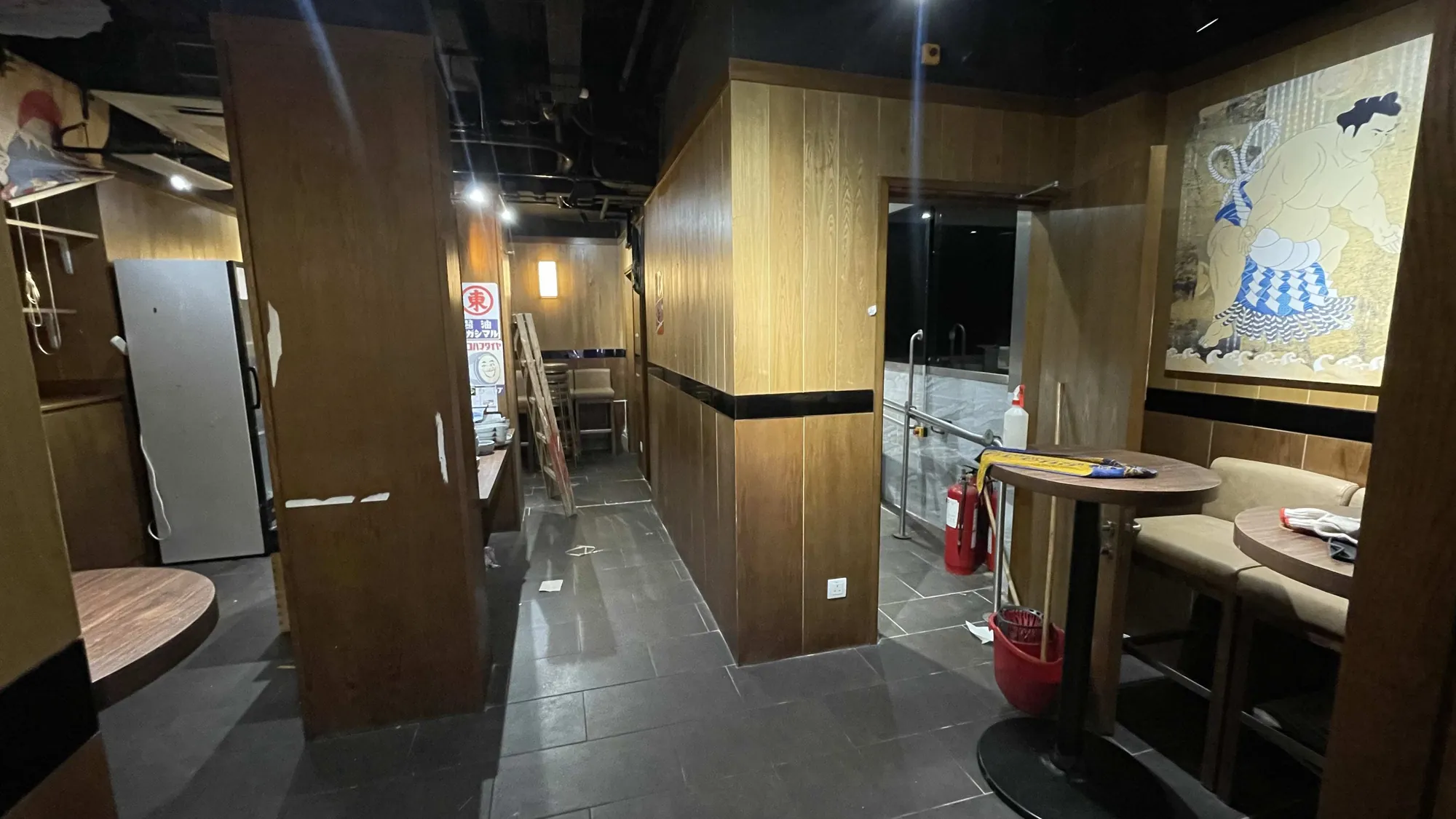 Ref#2995 offers an atmospheric space with wooden walls, a cozy table for two, sumo wrestler artwork, and convenient cleaning suppliesideal for anyone seeking to rent a unique restaurant or shop interior.