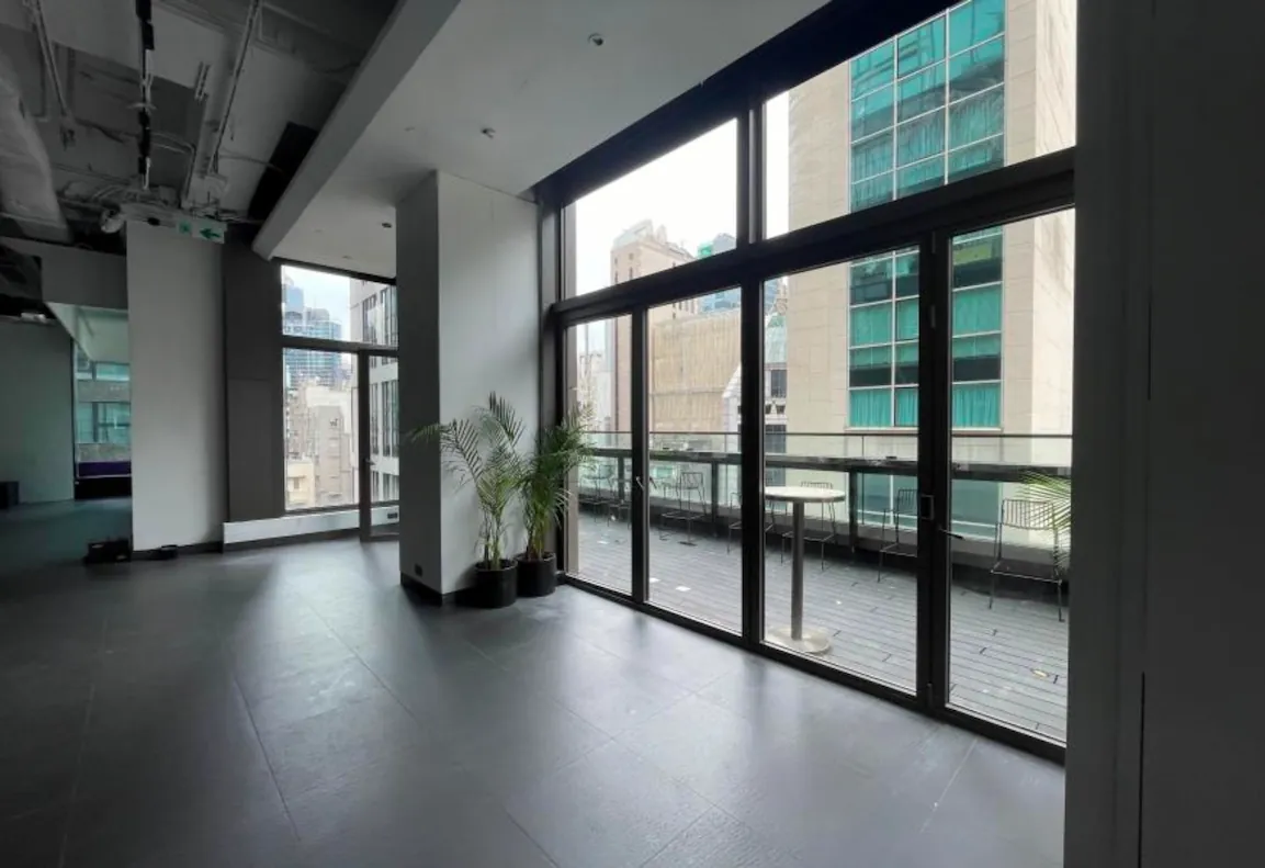 Ref#3601: Modern empty office space with large floor-to-ceiling windows, glass doors to a balcony, and bright tiled floors. Ideal for rent as office, shop, or restaurant. Two potted plants by the windows offer views of tall buildings.
