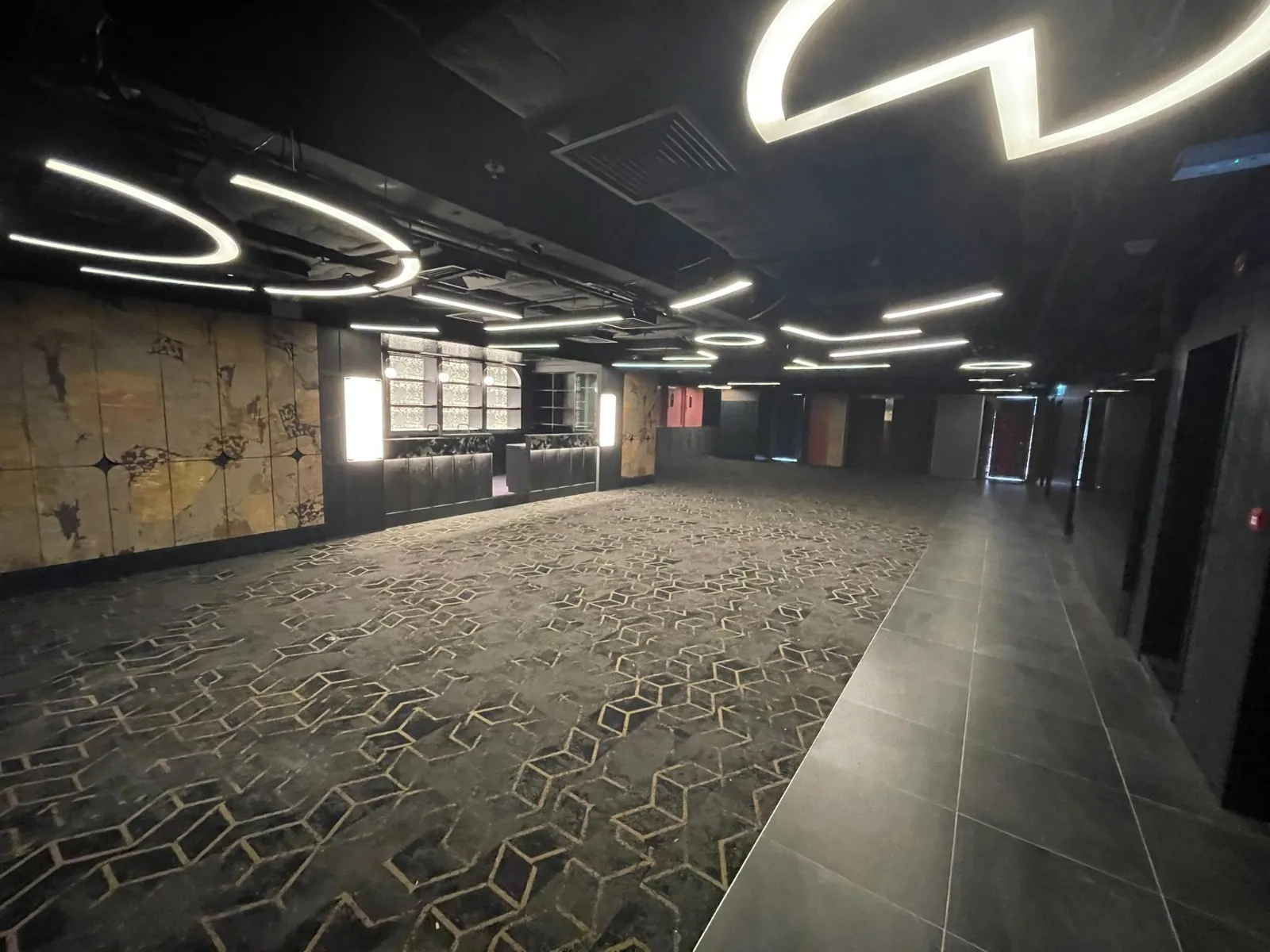 Ref#3602: A spacious, modern space perfect for a restaurant or office, with geometric carpet, abstract wall art, circular ceiling lights, partial tiled flooring, and a bar or counter area at the back.