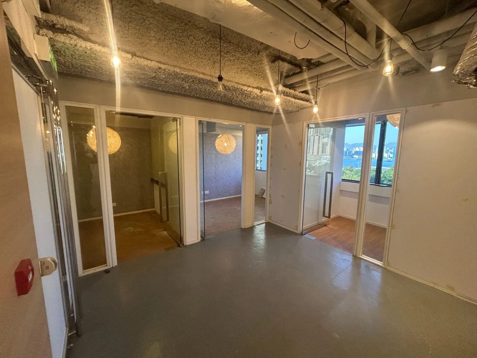 Ref#3605 features empty office space with gray floors, exposed ceiling pipes, and three glass-walled roomsperfect for office rental. Large windows offer city views and natural light; each room is illuminated by hanging lights and decorative lamps.