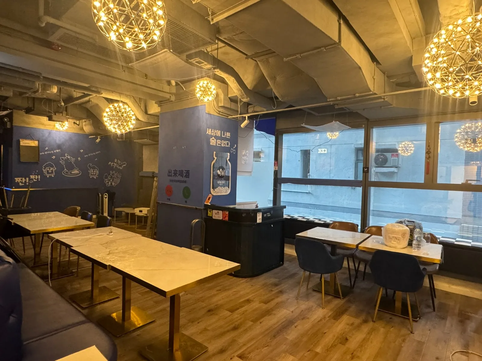Ref#3613: A cozy cafe featuring modern lighting, marble tables, blue chairs, and Korean wall art. Large windows provide natural light—perfect for a stylish and comfortable shop or restaurant rental.