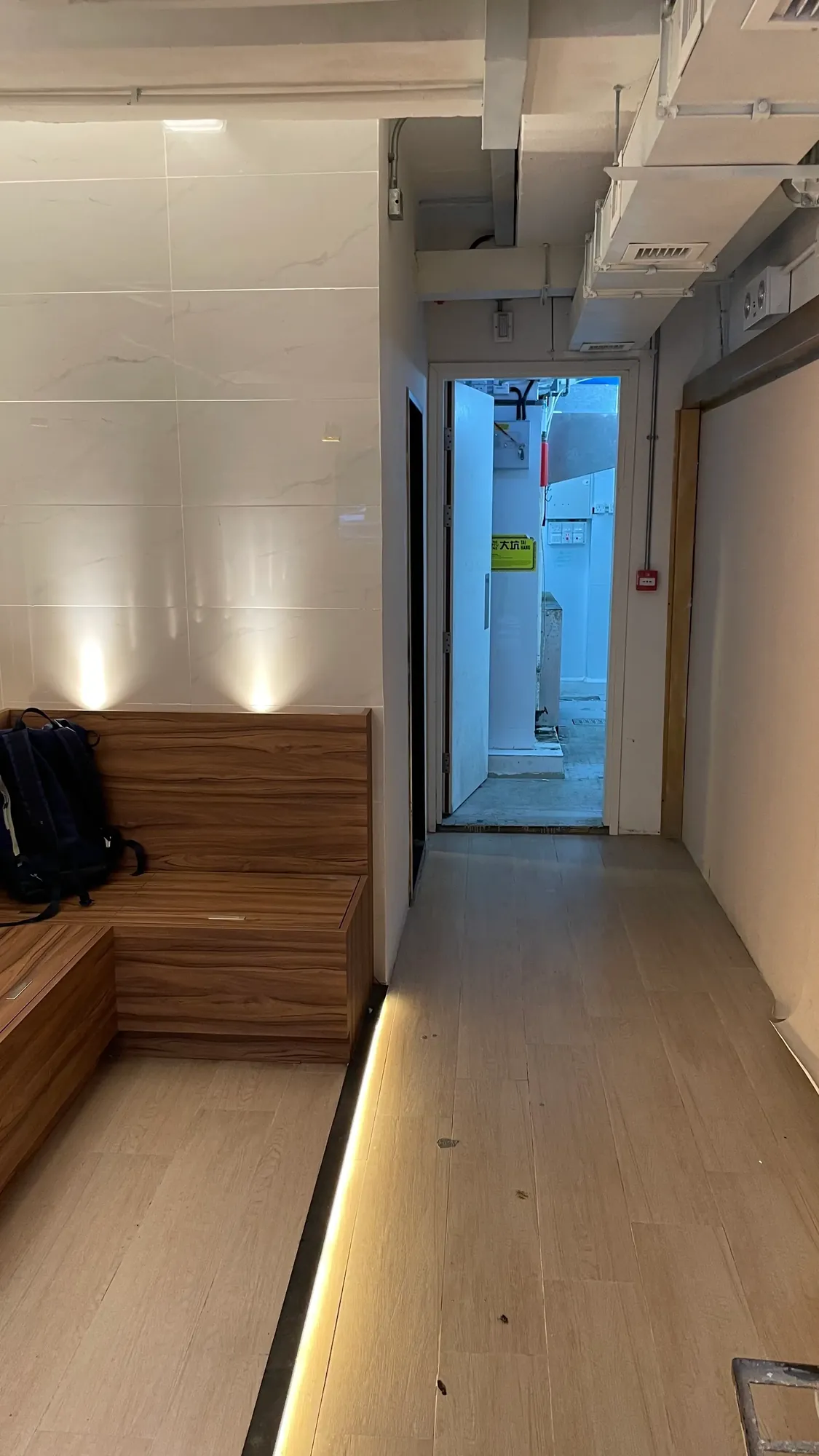 Ref#3647 features a modern hallway with wood-paneled seating and a backpack on the bench, offering a bright, light-filled space—ideal for those seeking to rent office or shop with exposed ceiling pipes.