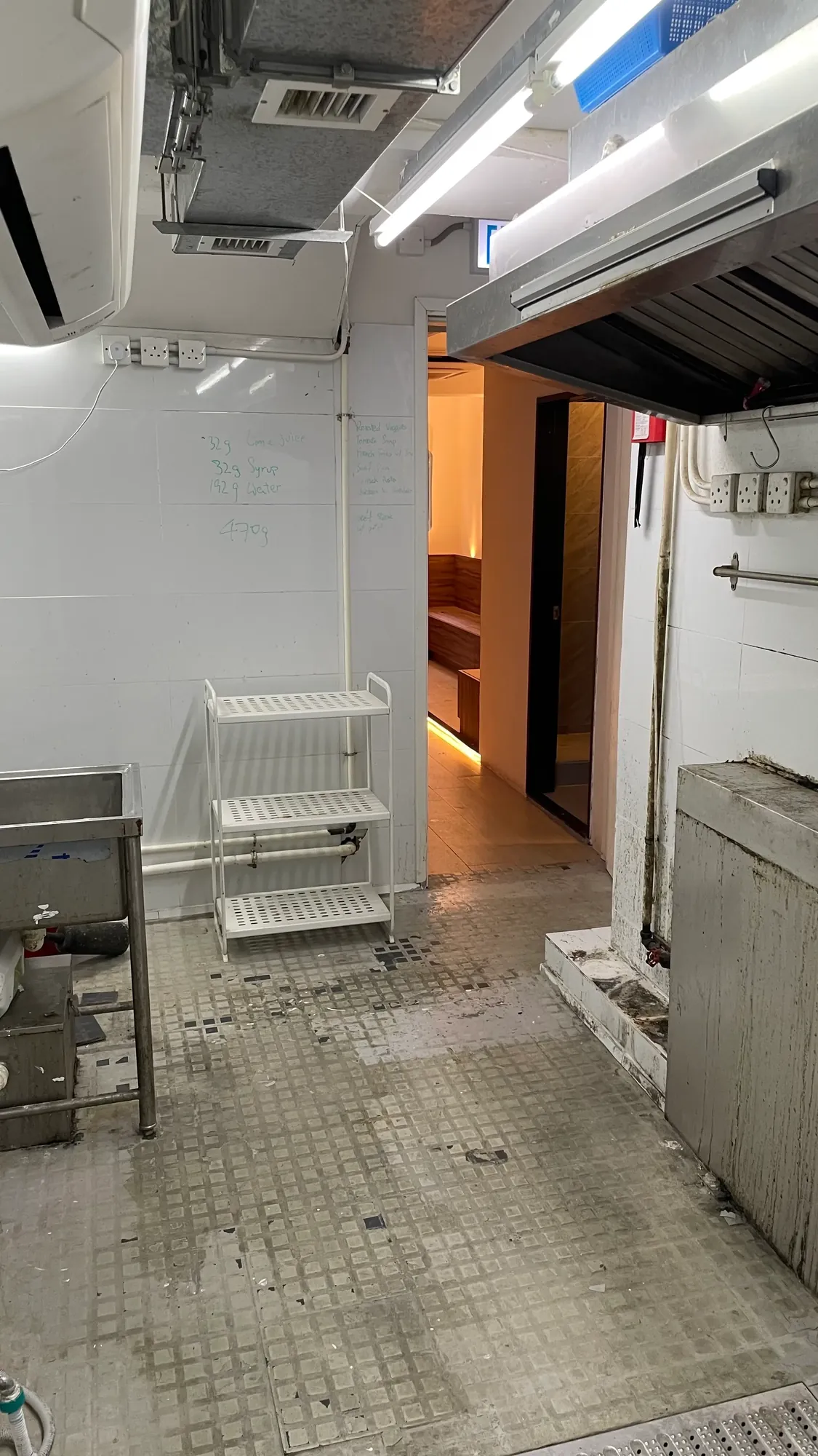 Industrial kitchen on Wun Sha Street with metal sink, white rack, tiled floor and a lit room visible in the background.