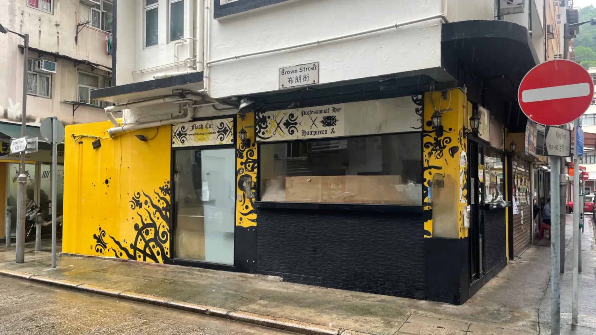 Ref#3648: Yellow and black restaurant with decorative patterns on an urban corner, featuring a large window, "Professional Bar Burgers &" sign, and wet pavementperfect for restaurant rental seekers.