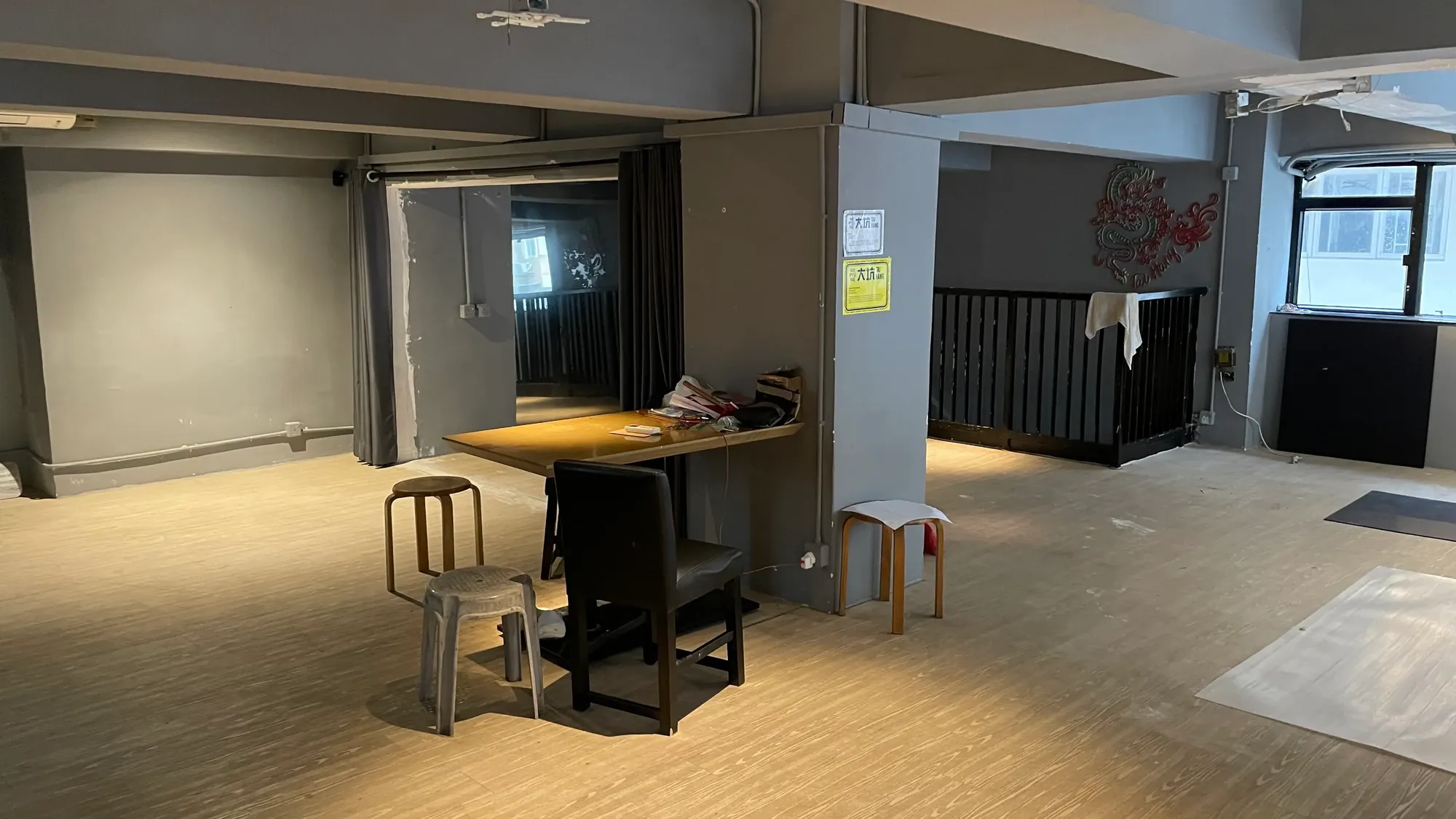 Ref#3650: Spacious, mostly empty room with gray walls and wooden floorsideal for an office, shop, or restaurant. Includes a table, 3 chairs, papers, partition, railing, and large windows that bring in abundant natural light.