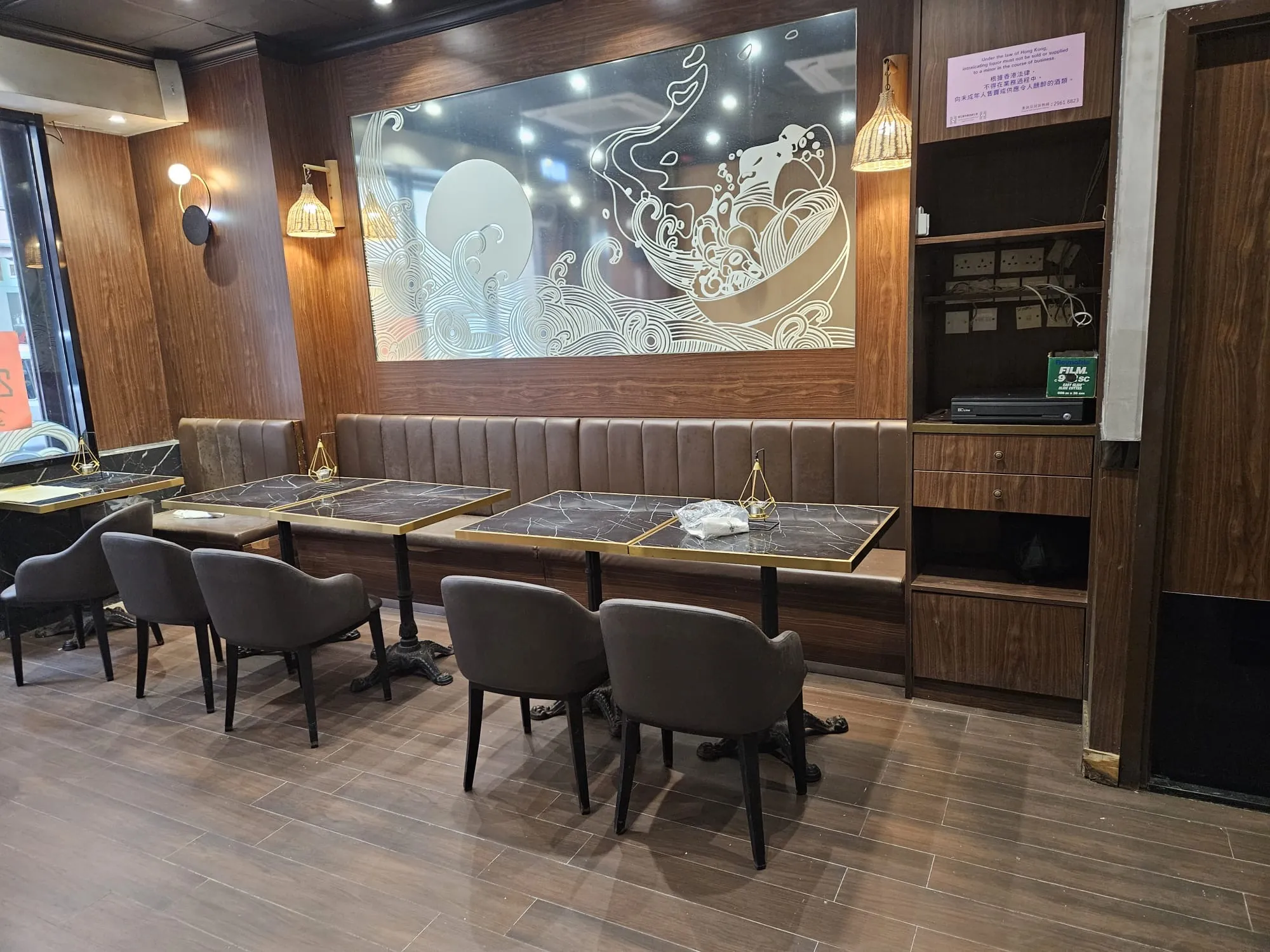 Restaurant interior in Kennedy Town with brown chairs, black tables, wave artwork, and an electronics shelf on Hau Wo Street.
