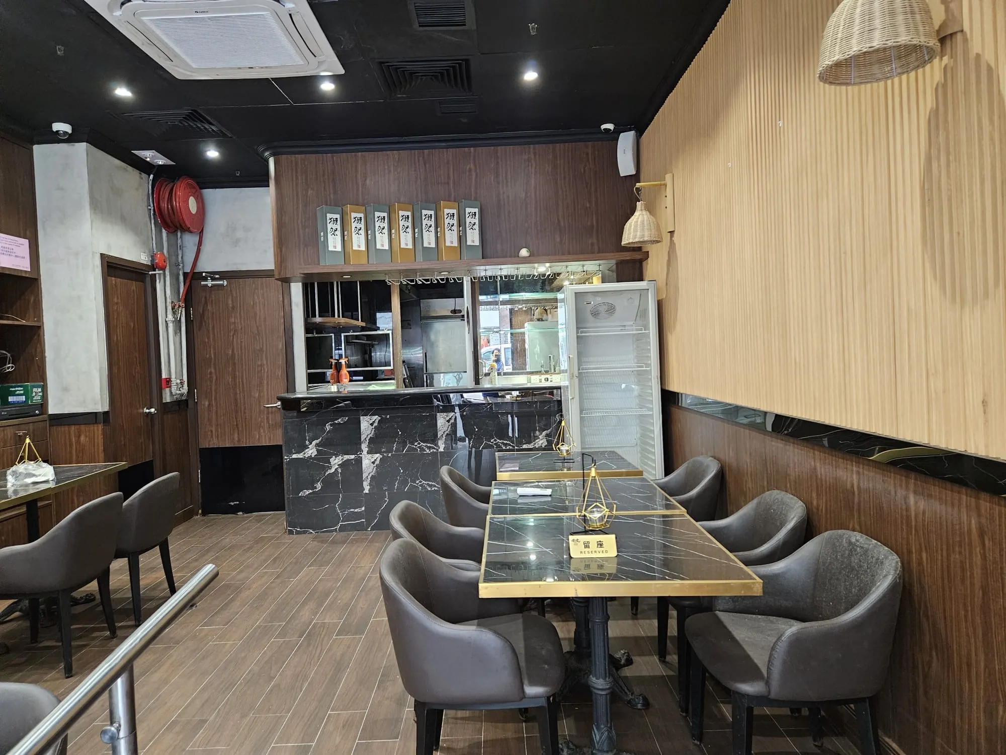 Modern restaurant interior on Hau Wo Street features dark tables, gray chairs, a marble counter, and an open refrigerator.