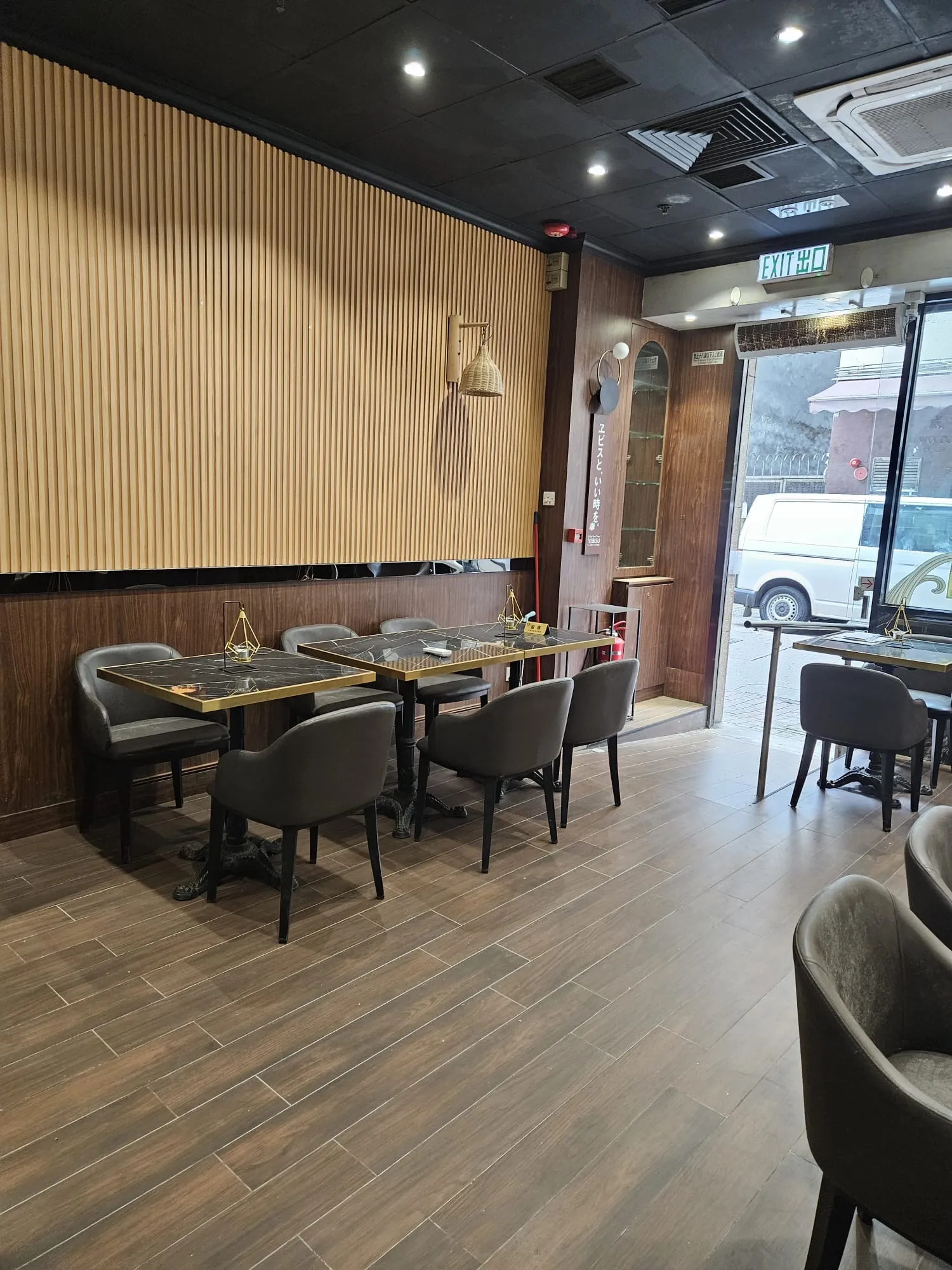 Modern cafe with wood floors and black ceiling on Hau Wo Street in Kennedy Town, empty tables by large windows.