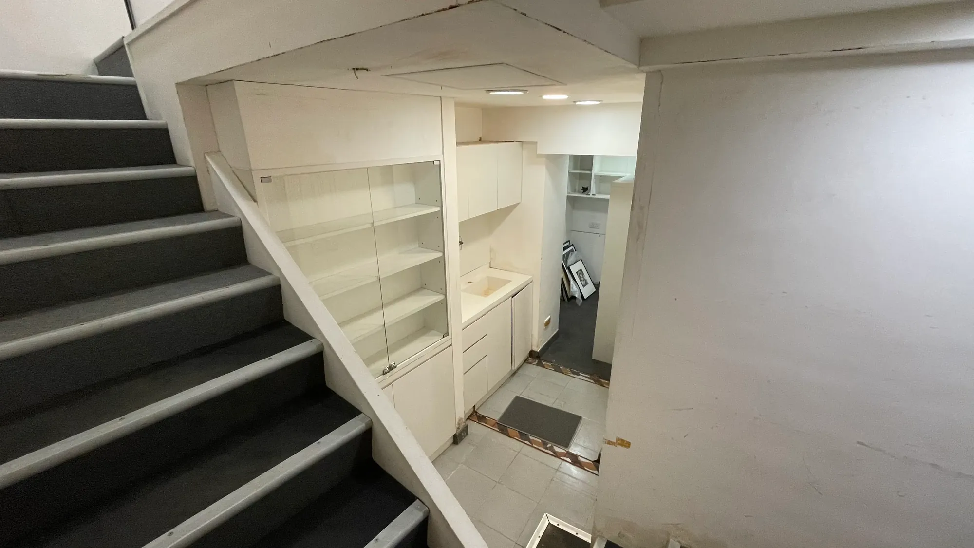 中環荷李活道一道樓梯，旁邊設有嵌入式置物架及小水槽，通往設有白牆的下層房間。