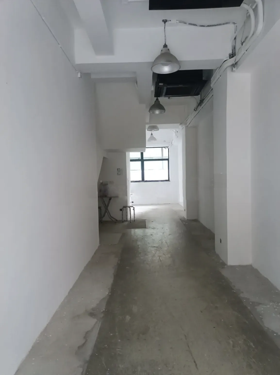 Narrow empty hallway on Staunton Street Central with white walls exposed pipes ceiling lights and a window at the end.