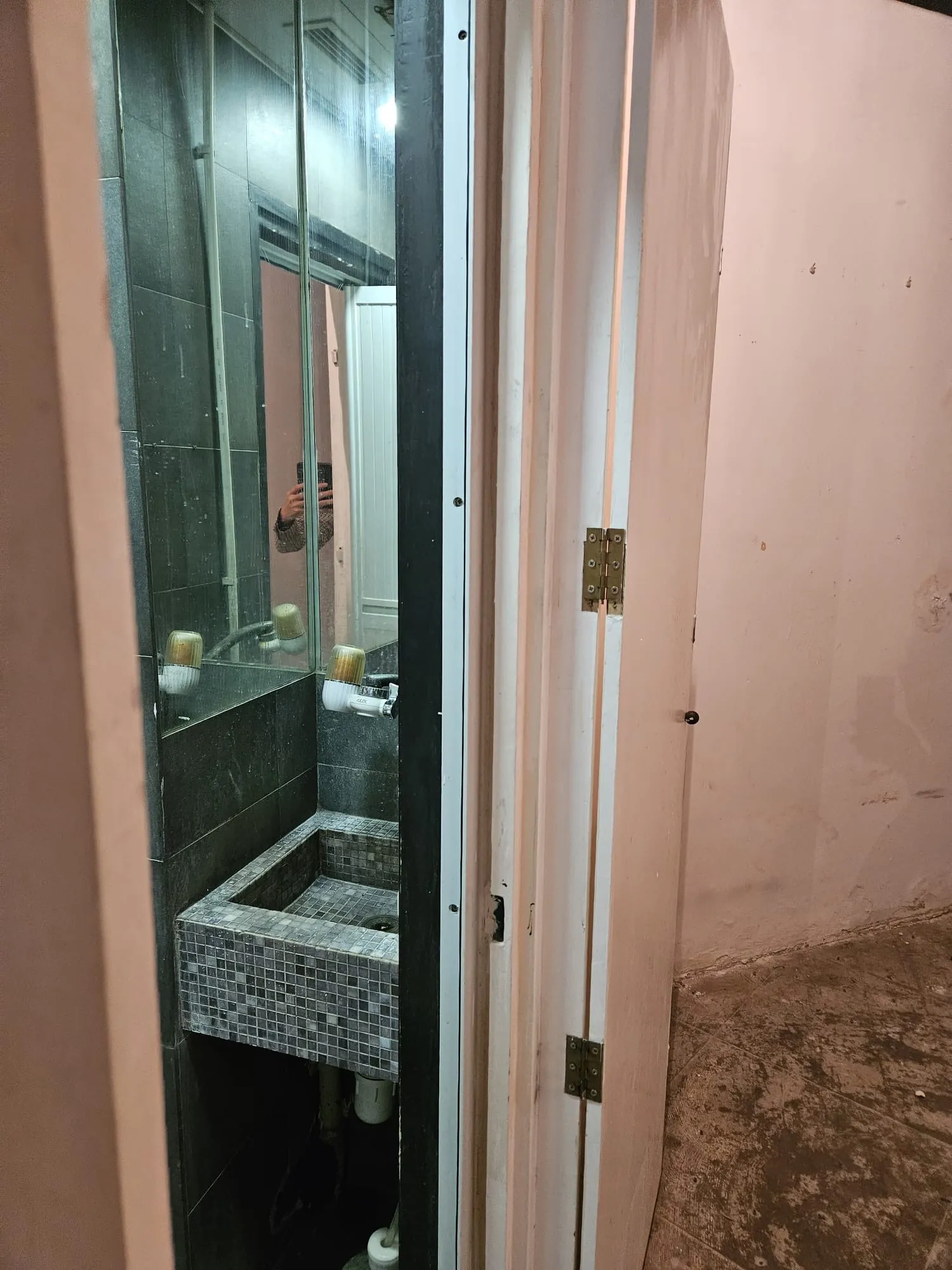 Open door shows tiled bathroom sink and mirror in Central; reflection includes striped shirt and camera flash.
