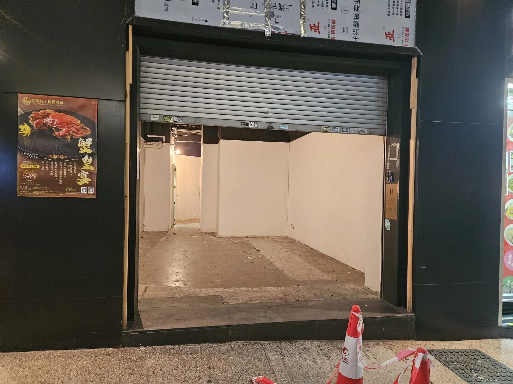 Shop on Lyndhurst Terrace, Central. Empty storefront, with white walls, partially open metal shutter, and two orange cones outside.