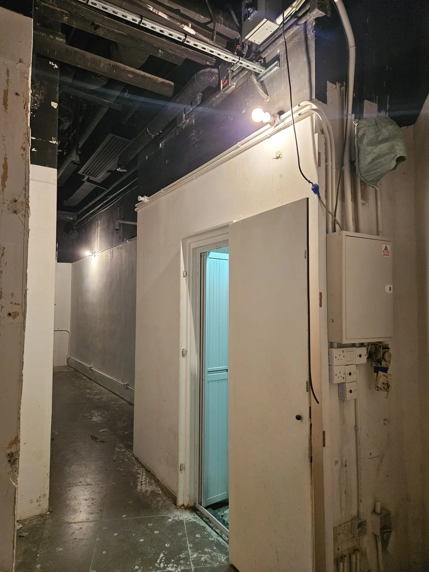 Dimly lit hallway at Lyndhurst Terrace in Central with exposed wiring, blue-lit open door, and visible electrical panels.