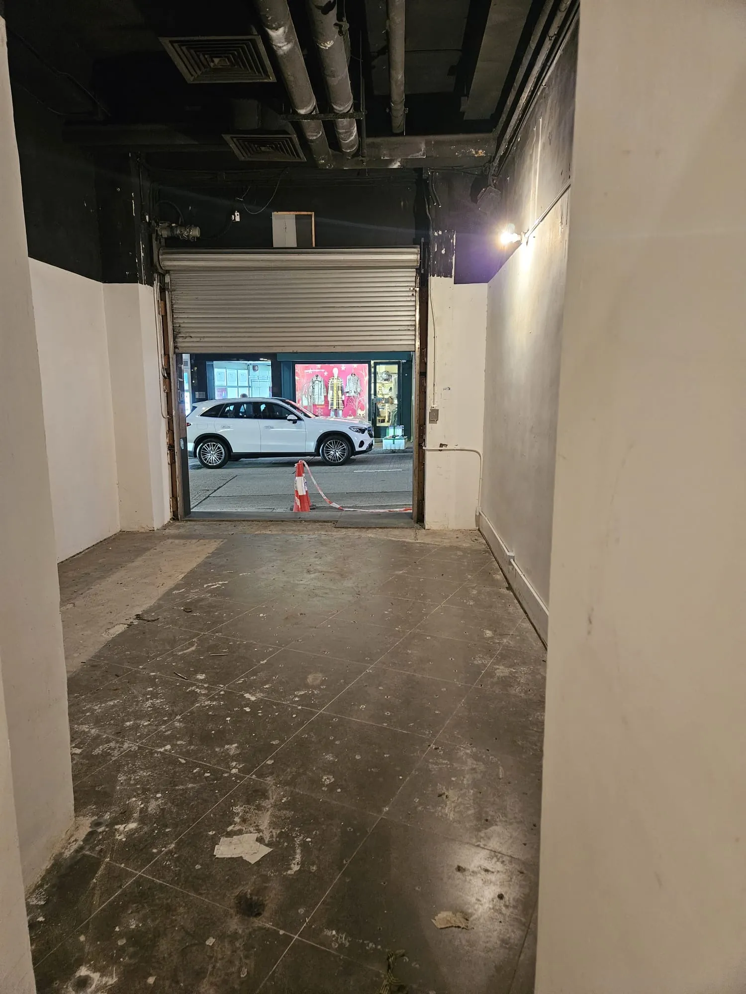 Empty room with tiled floor and open roll-up door on Lyndhurst Terrace, showing a white car and orange cone outside.