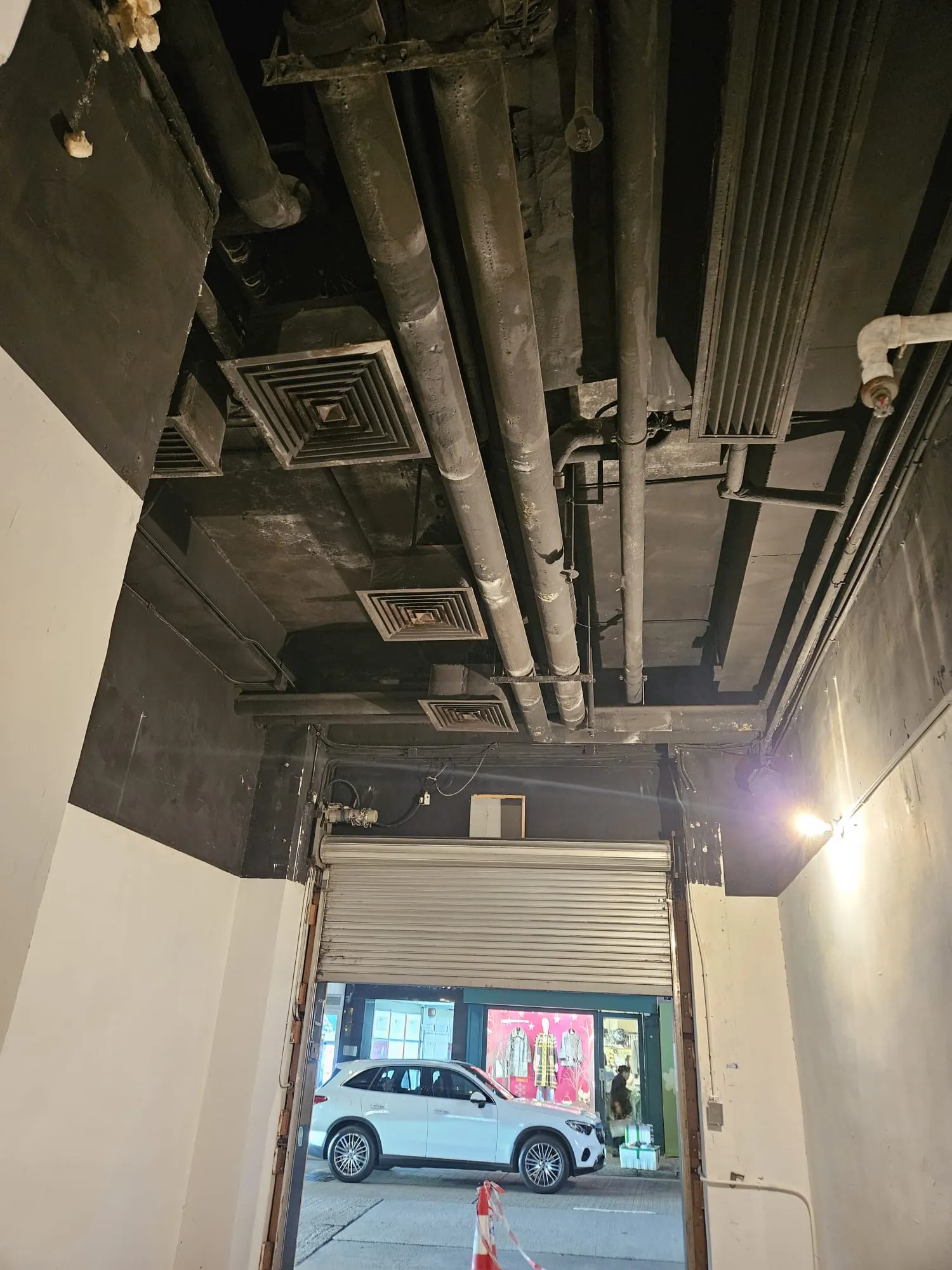 Exposed black pipes and vents on ceiling above open garage door in Lyndhurst Terrace Central with white car parked outside.