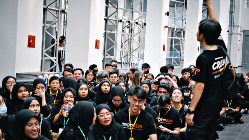 TROOPERS part-time crew sitting in a large hall during an event orientation, wearing branded TROOPERS shirts.