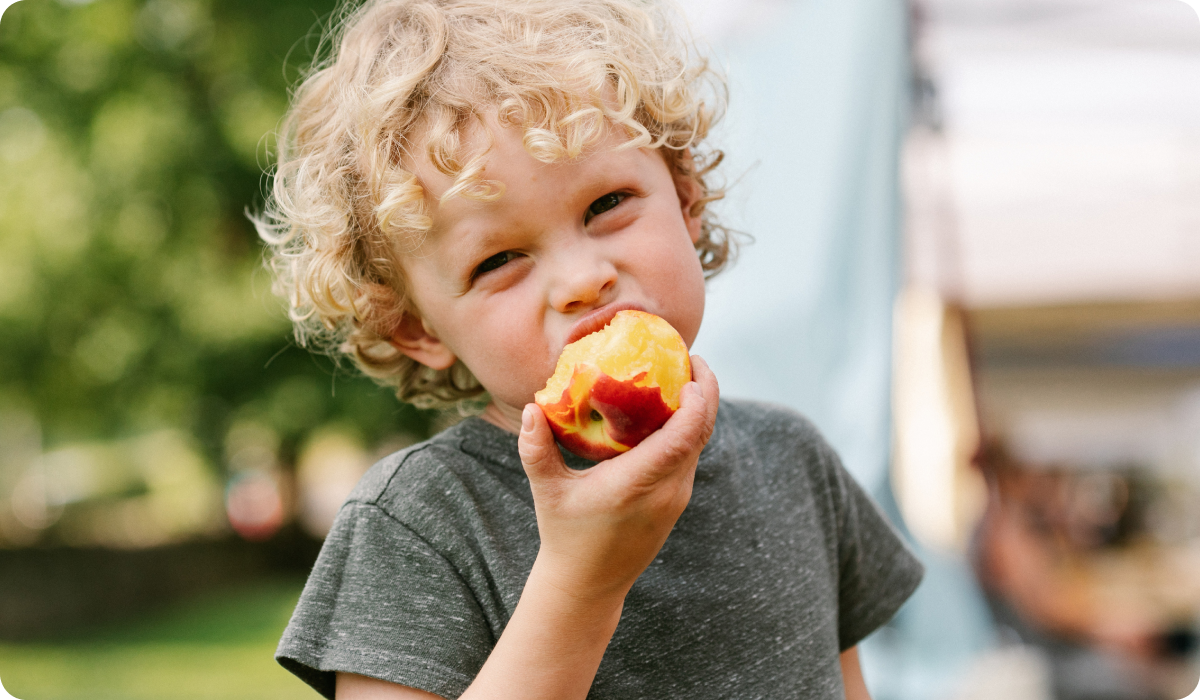 Young child eating a juicy fresh peach outdoors showcasing seasonal summer fruit enjoyment