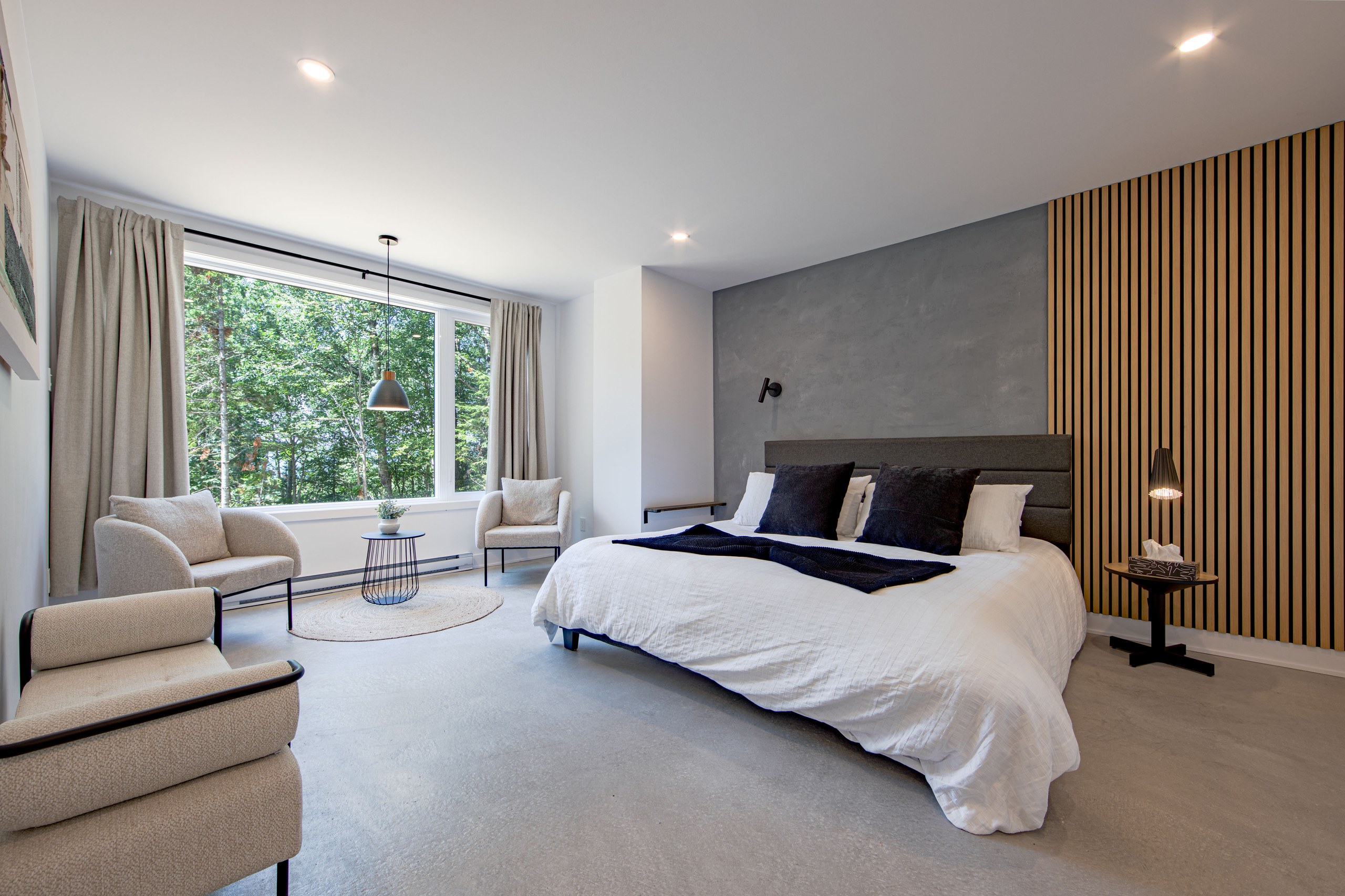 Chalet Le Boréal chambre principale mur de béton ciré gris panneau de lattes de bois et grande fenêtre sur la forêt