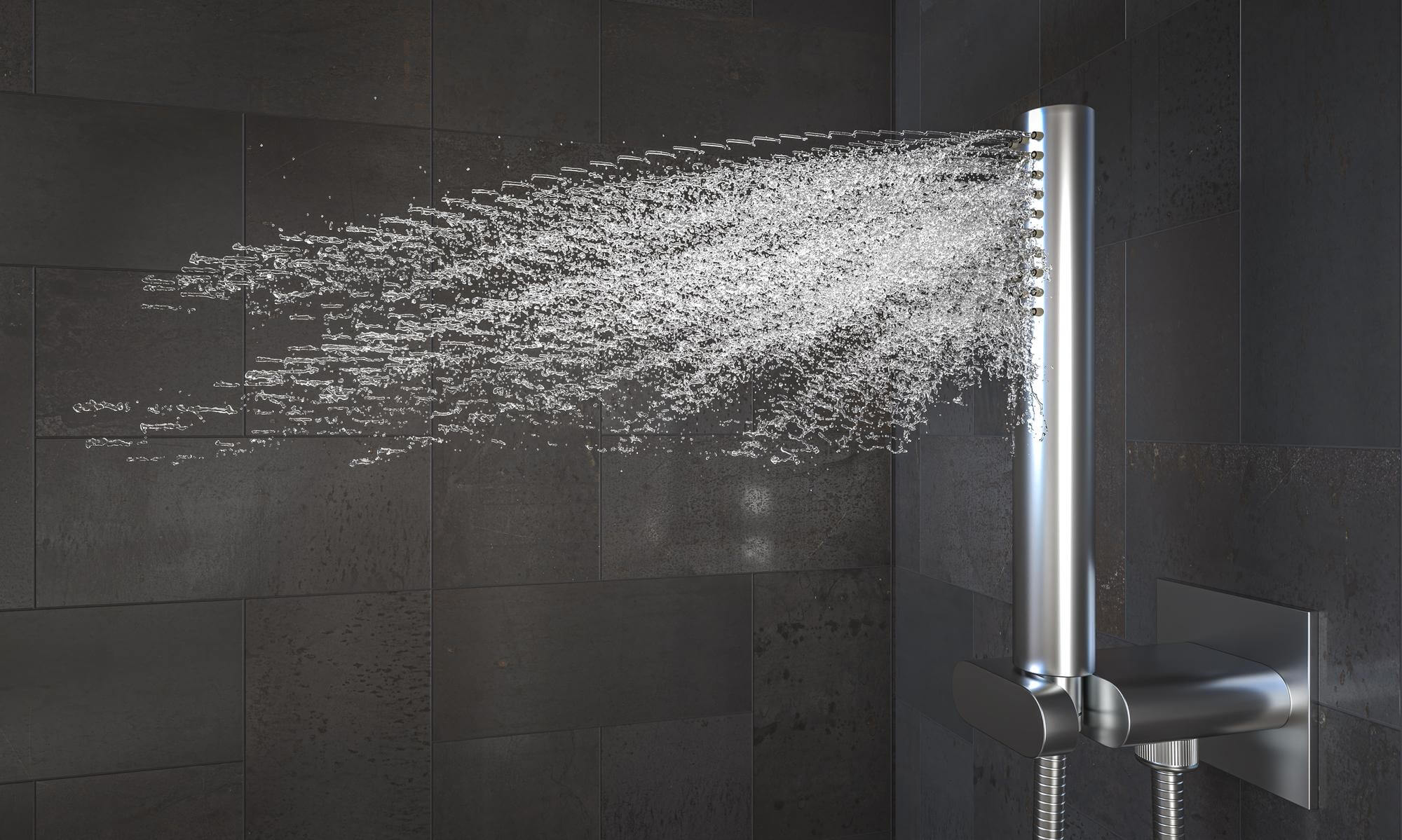 Modern silver handheld showerhead spraying water against a dark tiled wall.