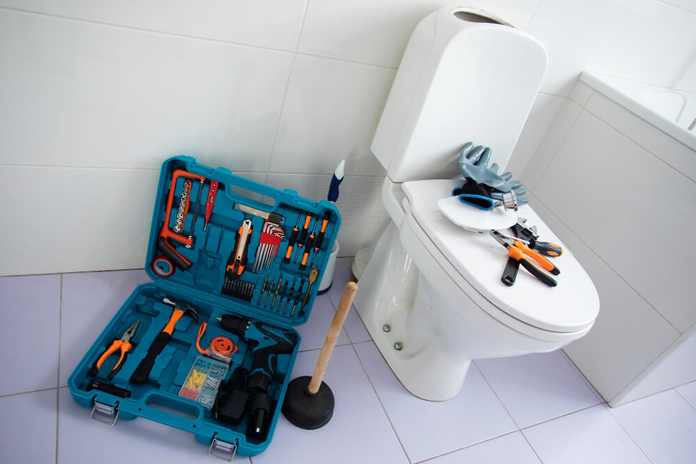 Open blue toolbox with various plumbing tools next to a white toilet with tools and gloves on the closed lid.