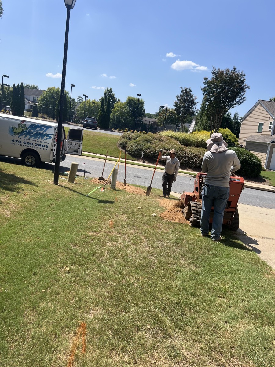Two workers installing water lines on a grassy residential front yard with digging equipment and tools beside a service van.