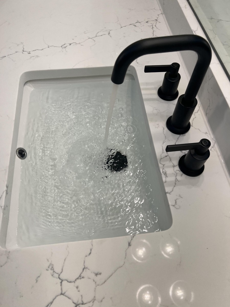 Modern rectangular white sink with water running from a black faucet set on a white marble countertop with subtle gray veining.