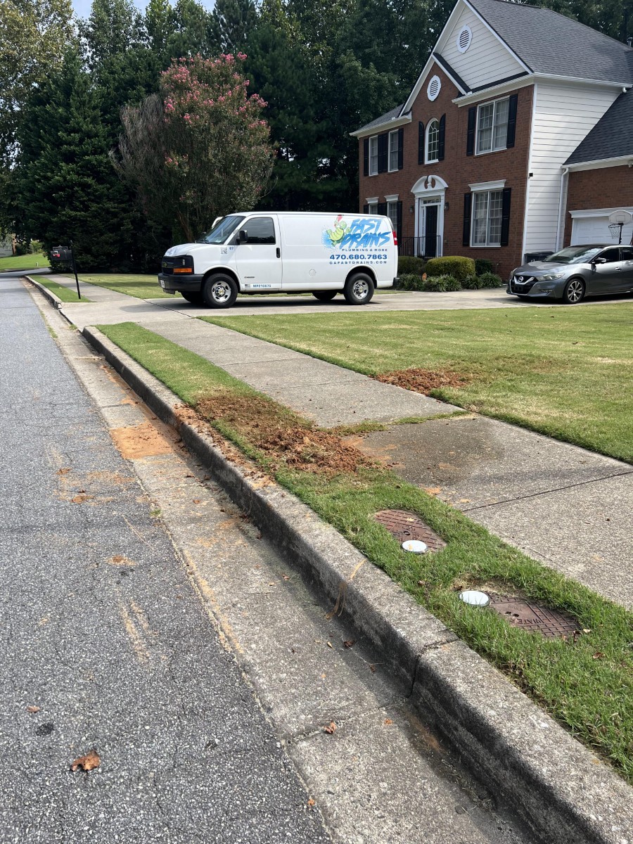 White Fast Drains Plumbing van parked in the driveway of a two-story brick and white siding house with a well-maintained lawn.