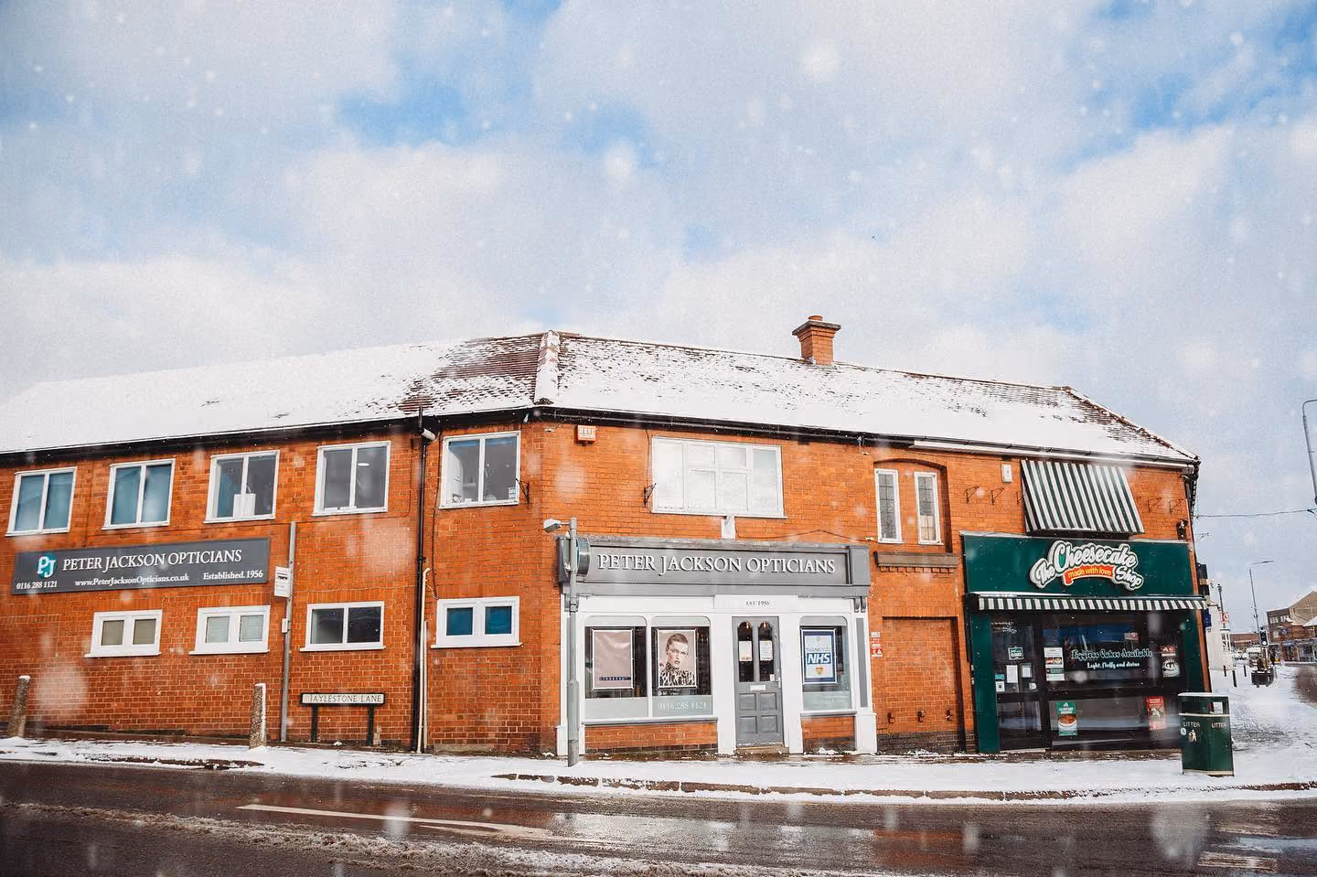 Red brick building with Peter Jackson Opticians storefront that is covered in snow