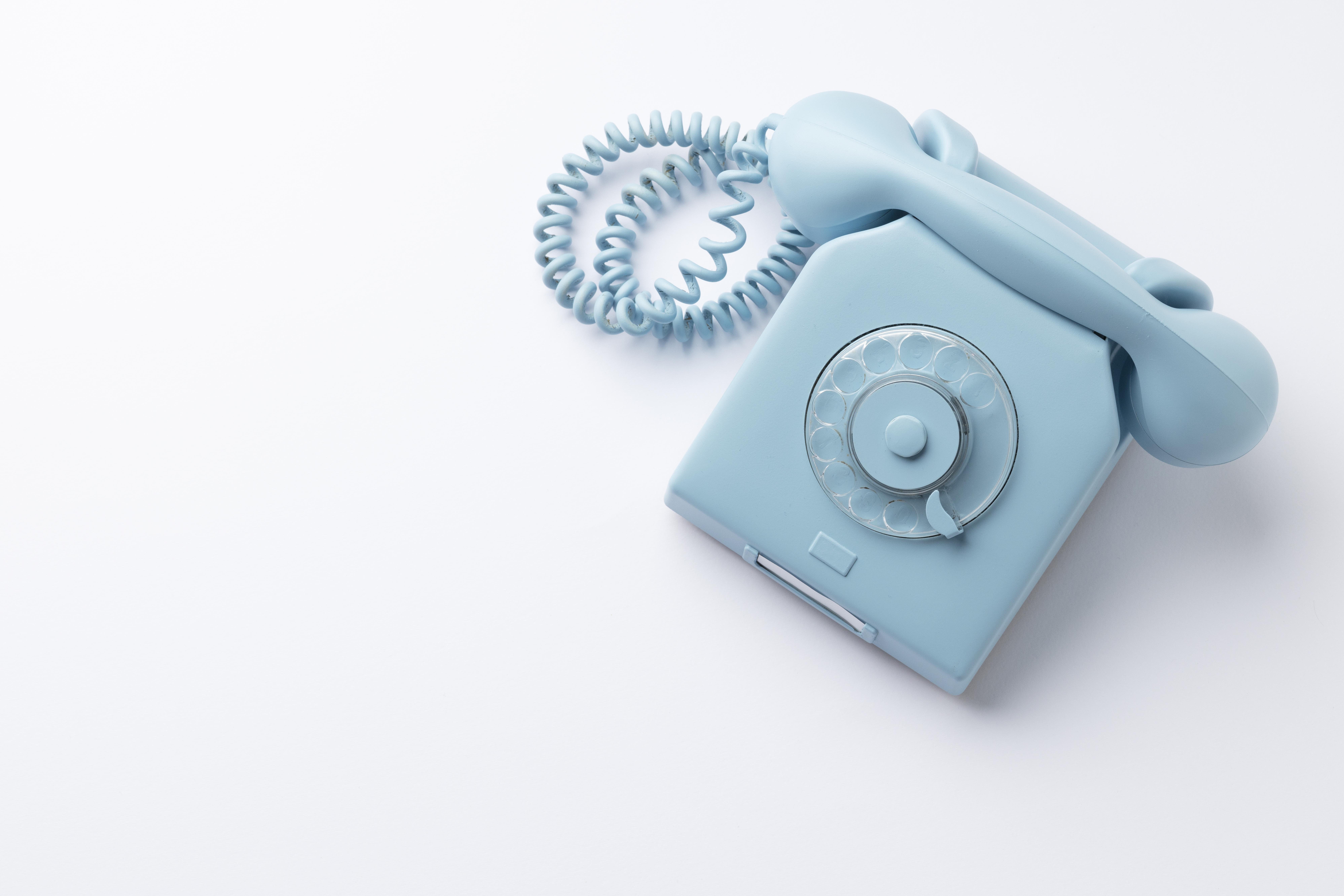 Light blue vintage rotary telephone with spiral cord on white background