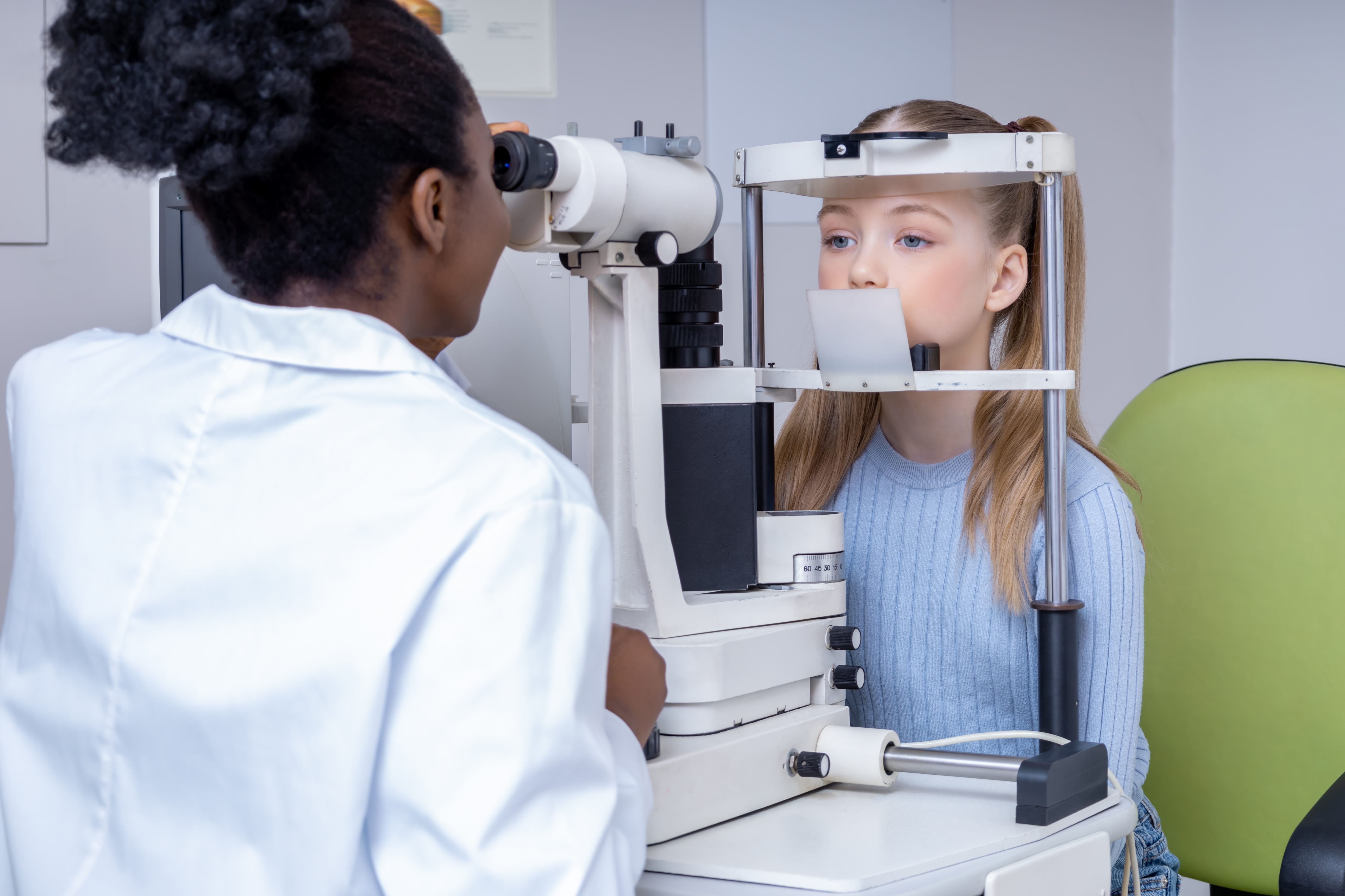 Optometrist using phoropter to test child's vision during eye examination