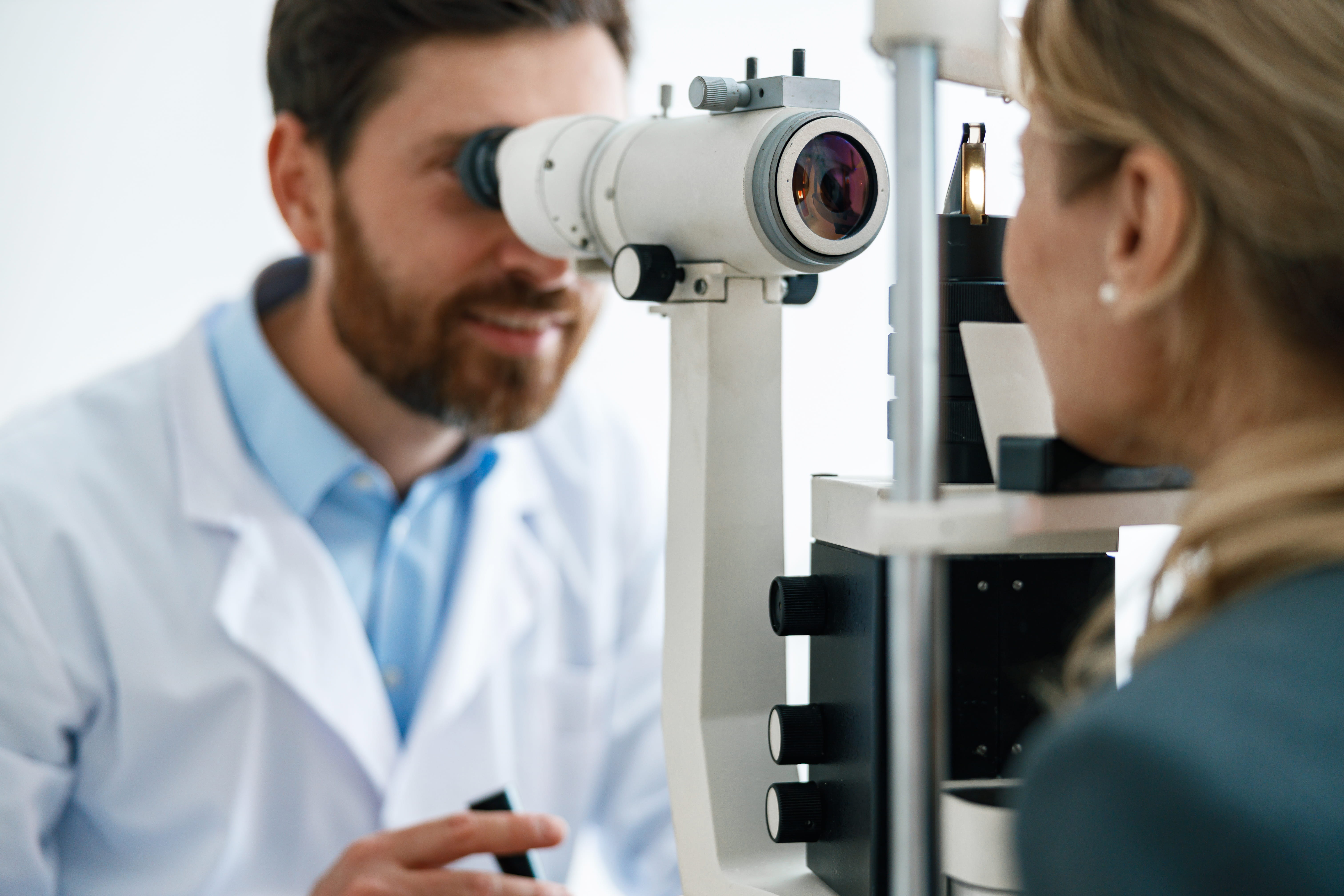 Optometrist conducting eye exam with phoropter on female patient